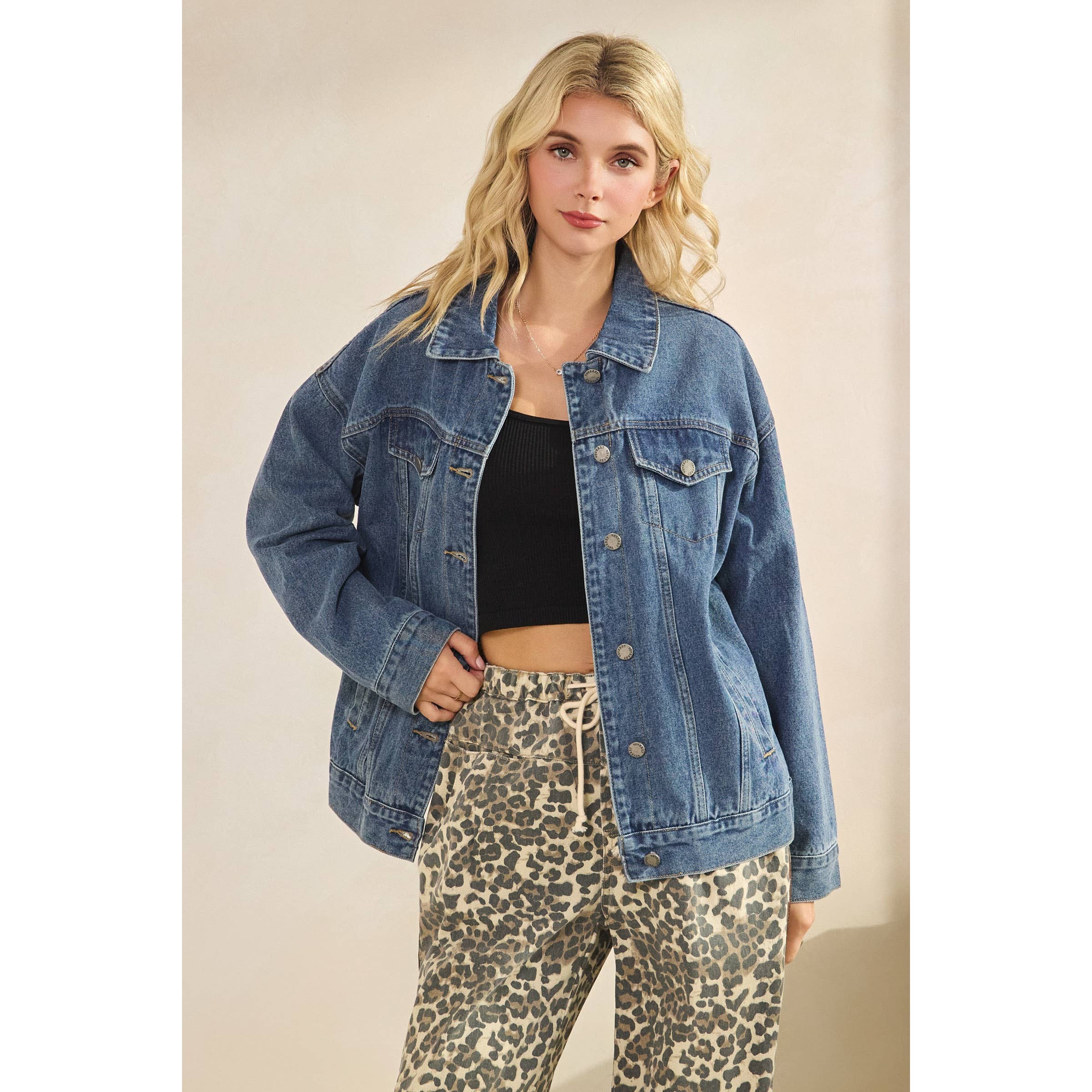 Woman wearing a denim jacket and leopard print pants against a plain background