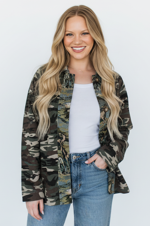 Woman wearing a camouflage jacket over a white shirt and blue jeans on a white background