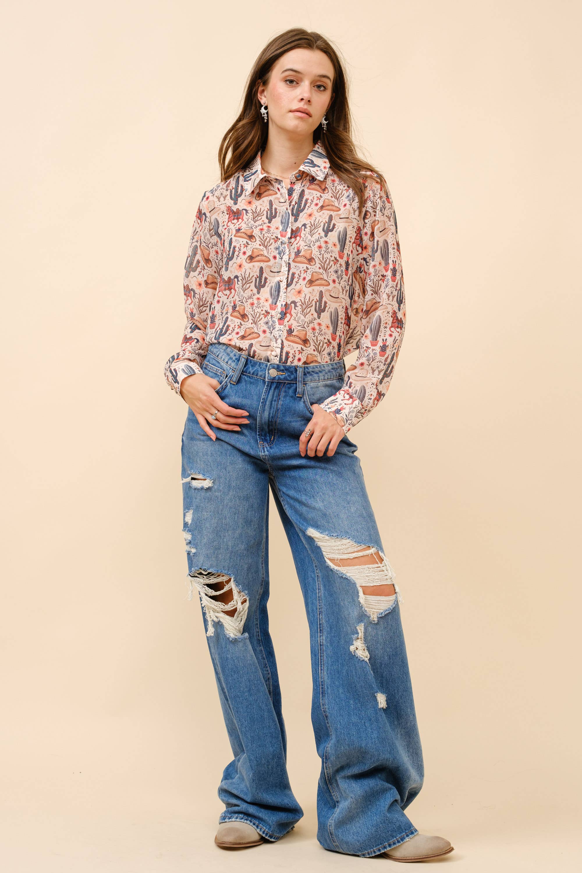 Woman wearing a patterned blouse and ripped jeans on a beige background
