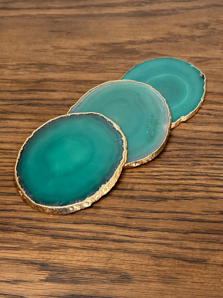 Three teal coasters with gold edges on a wooden surface