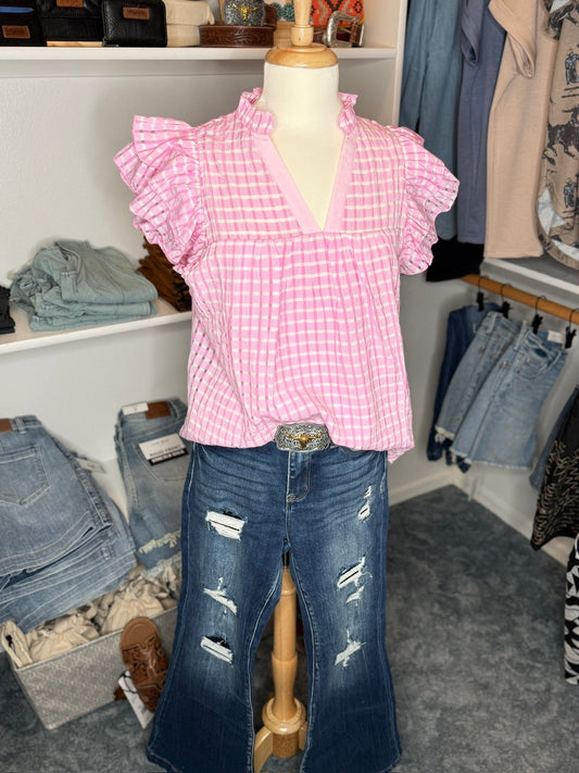 A mannequin displaying a pink v-neck gingham blouse with fluttery cap sleeves and a pair of blue denim jeans.