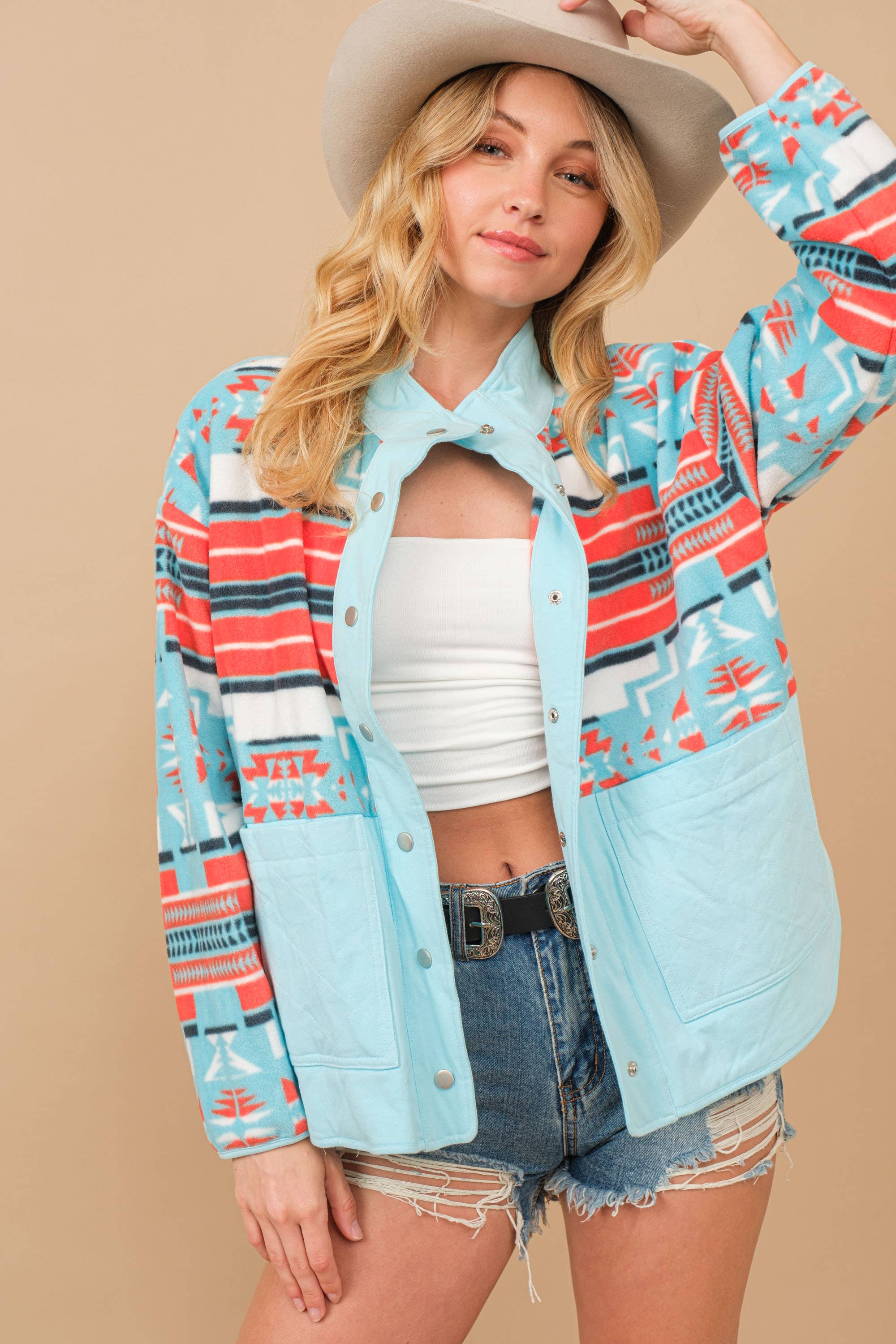 Woman wearing a colorful patterned jacket over a white top and denim shorts on a beige background