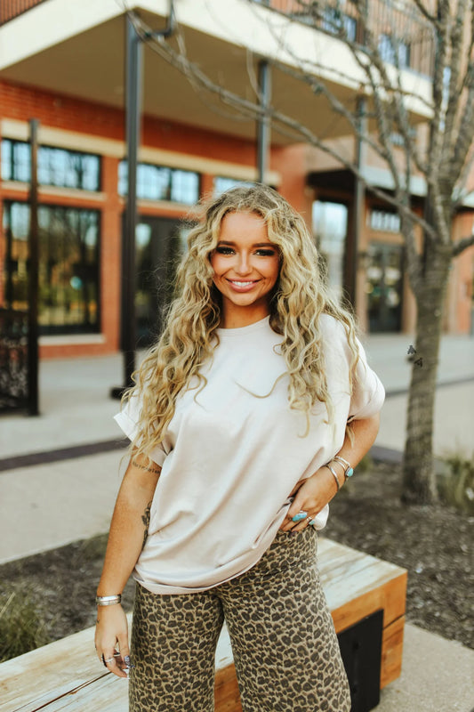 A woman wearing a white short sleeve t-shirt and leopard print pants, standing outdoors.