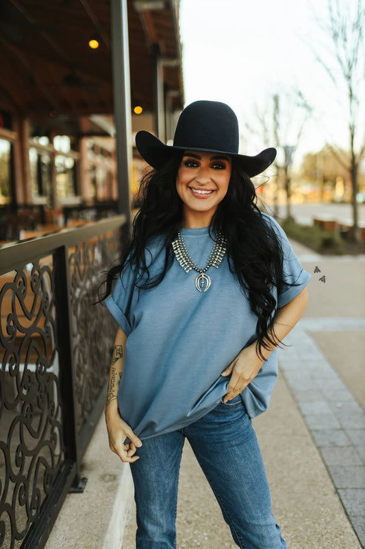 A person wearing a blue t-shirt and a black cowboy hat standing outdoors.