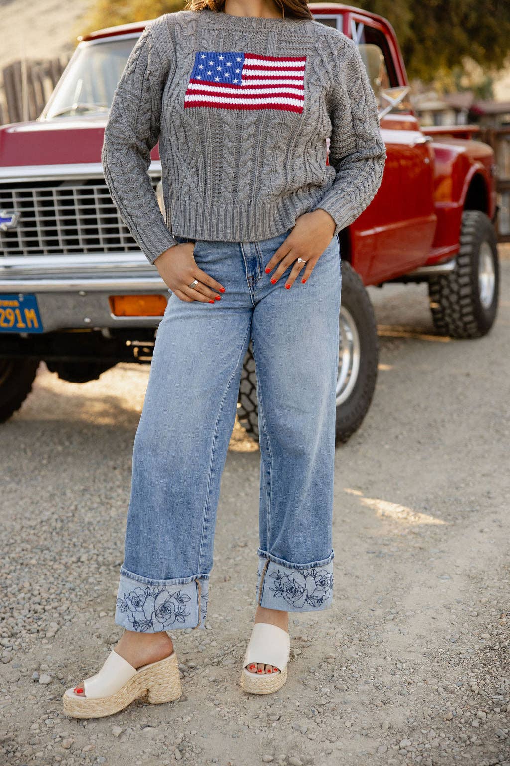 Person wearing a sweater with an American flag patch, standing in front of a red truck.