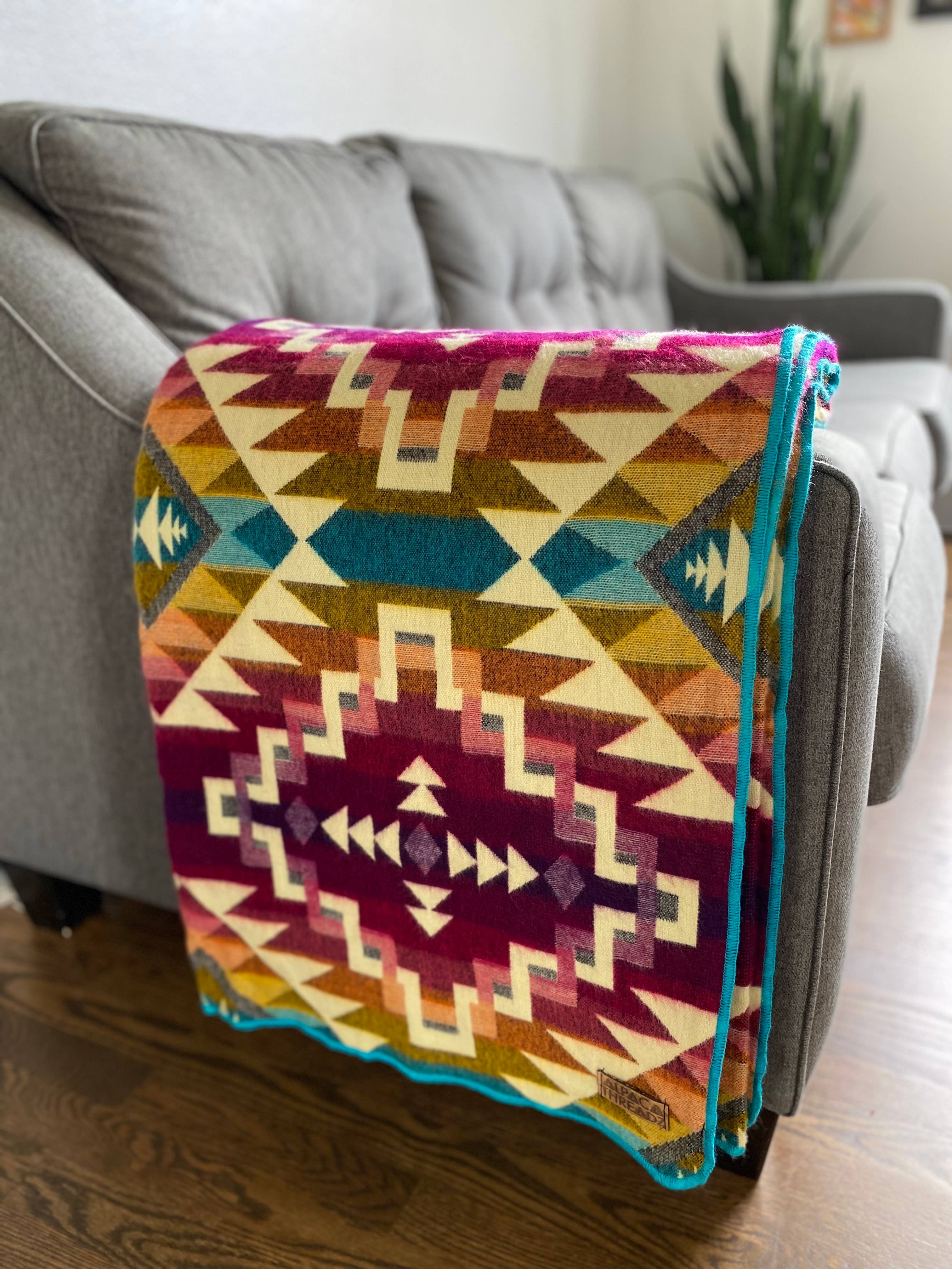 Colorful patterned blanket draped over a gray sofa in a living room.