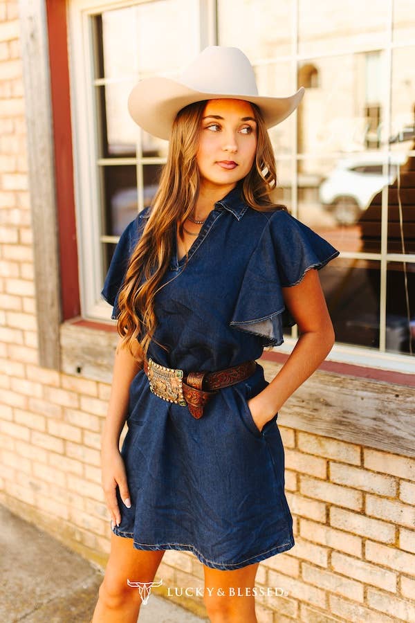 Woman wearing a blue dress and cowboy hat standing in front of a brick building.