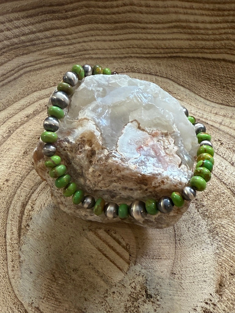 Bracelet with green and silver beads on a crystal stone against a textured beige background