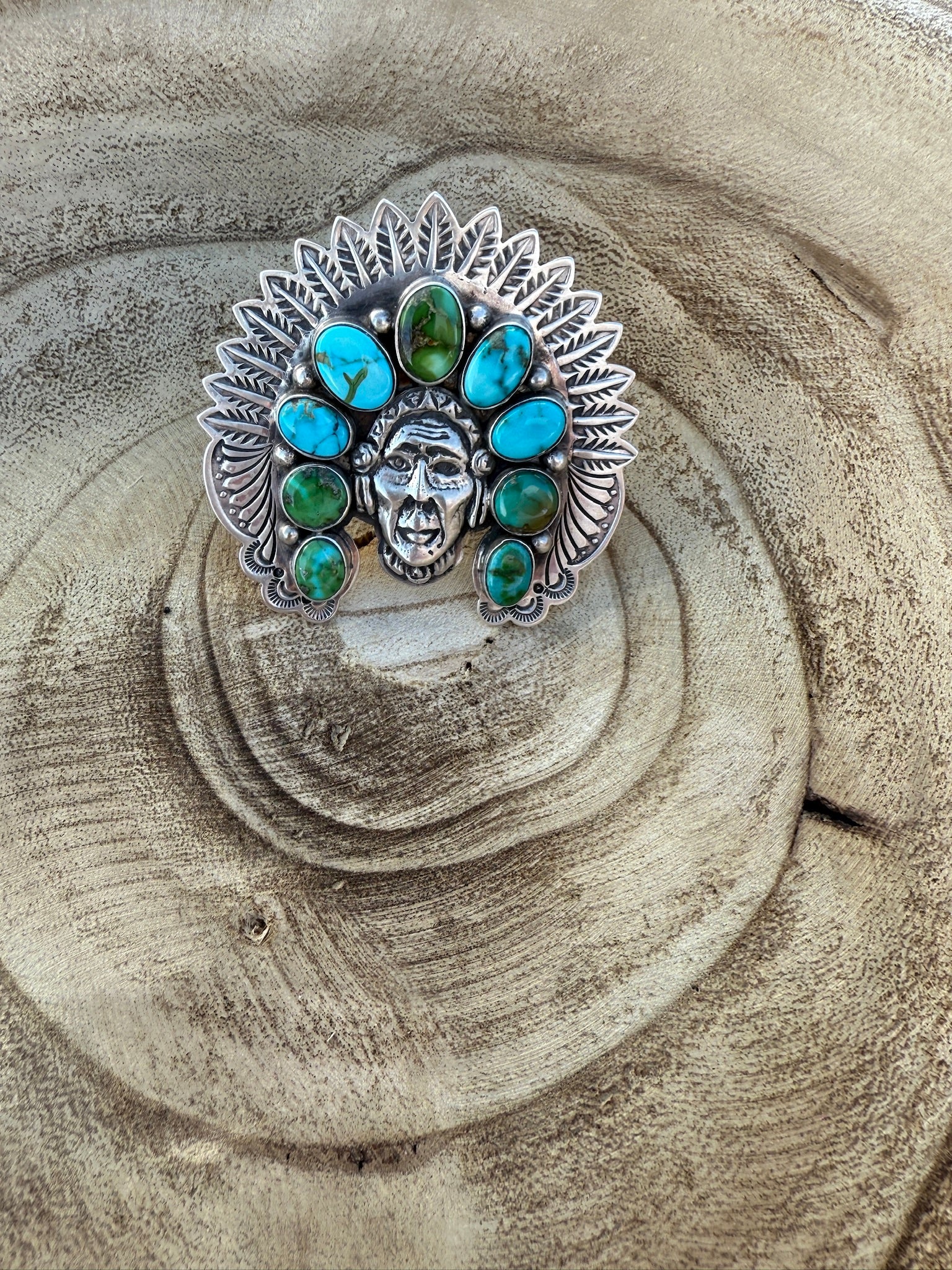 Silver ring with turquoise and green gemstones on a wooden surface