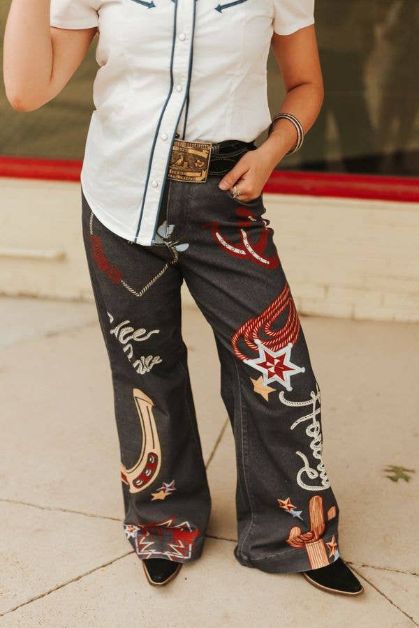 Person wearing black jeans with colorful embroidery and a white shirt.