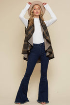 Woman wearing a plaid vest, white shirt, and blue jeans against a beige background