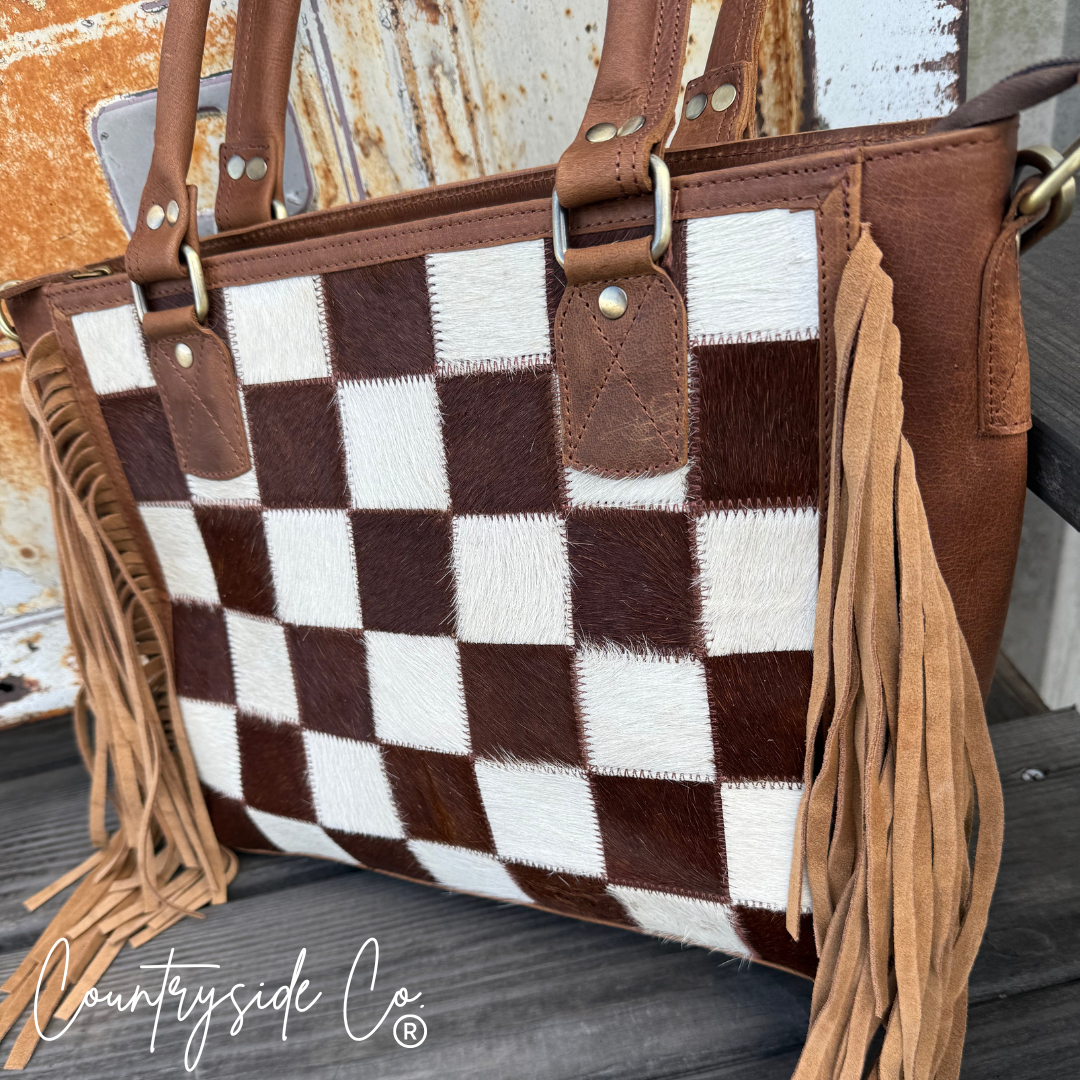 Brown and white checkered handbag with fringes on a wooden surface, featuring 'Countryside Co' branding.