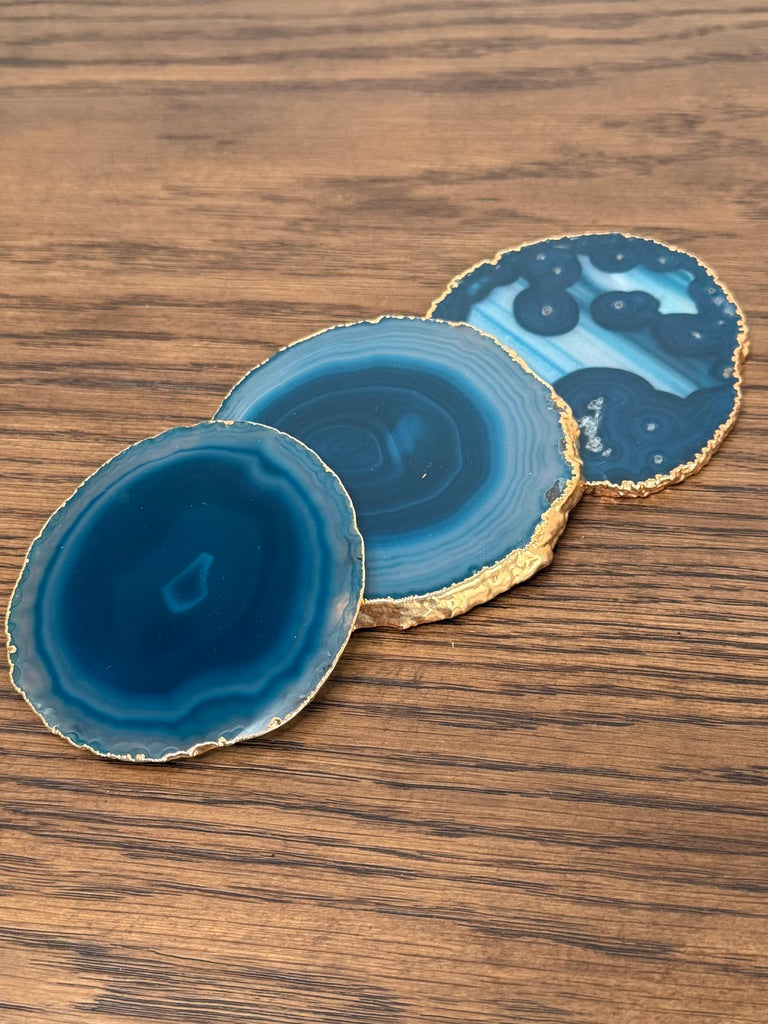 Three blue agate coasters with gold edges on a wooden surface