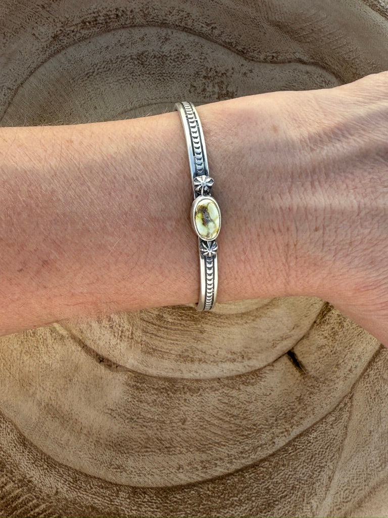 Silver bracelet with a yellow gemstone on a wrist against a sandy background