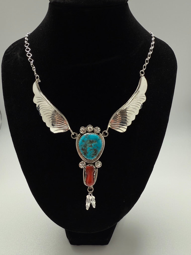 Necklace with silver wings and turquoise and red stone on a black bust