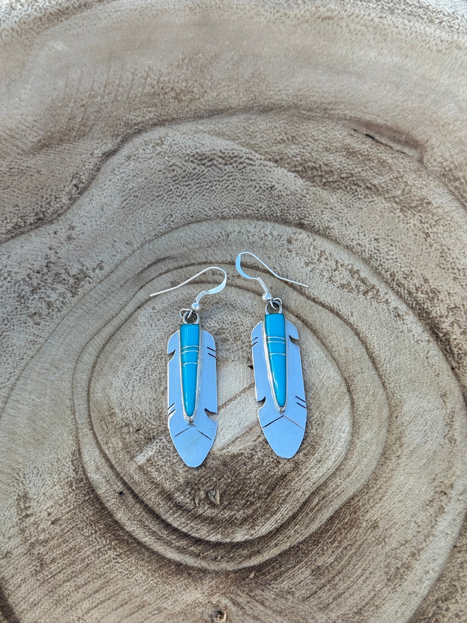 Blue feather-shaped earrings on a sandy surface