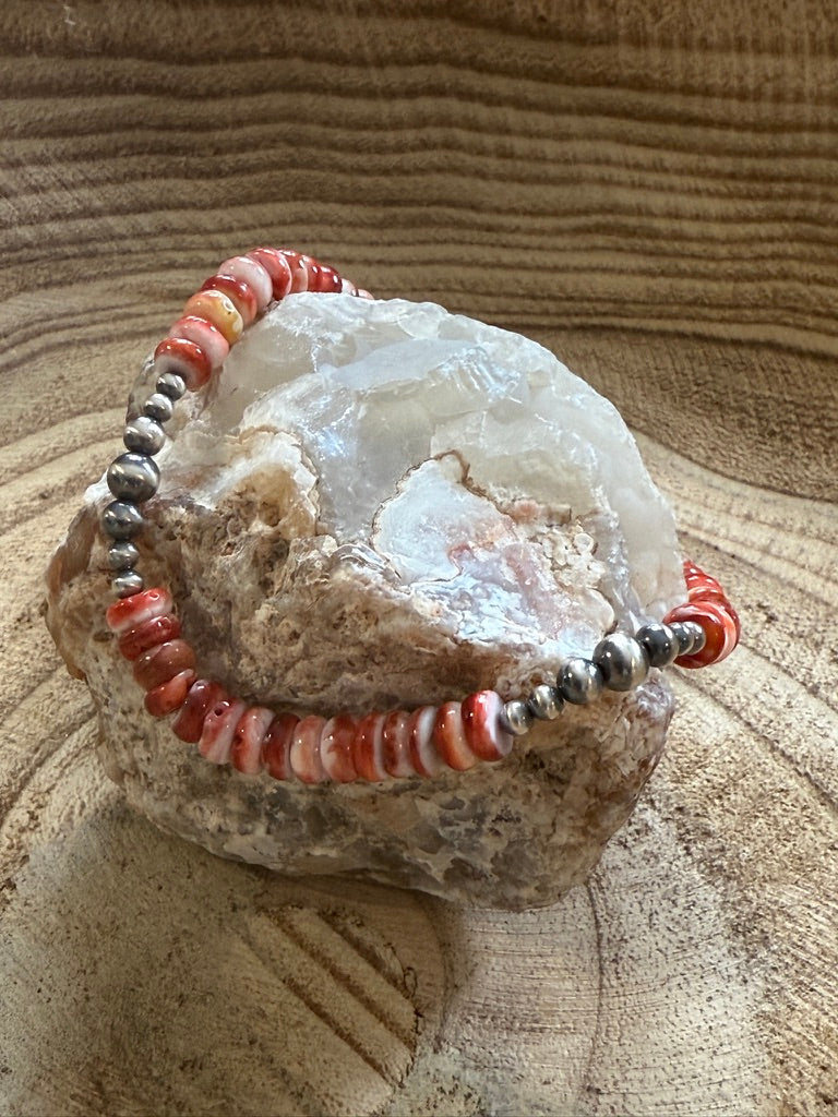 Bracelet with red and silver beads on a textured stone surface