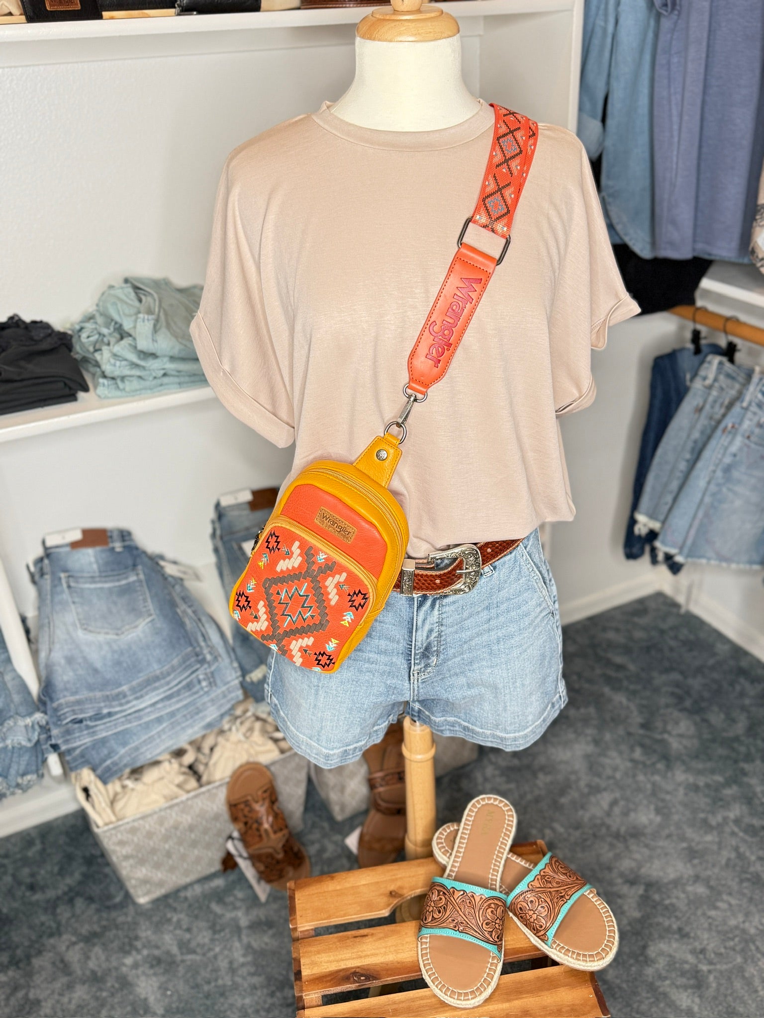 Mannequin wearing a beige shirt, denim shorts, and orange crossbody bag in a store setting.