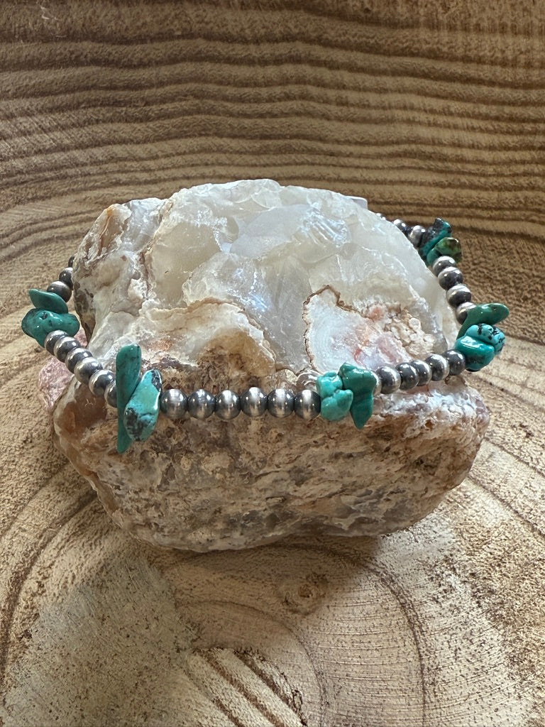 Turquoise and silver beaded bracelet on a rock with a textured beige background