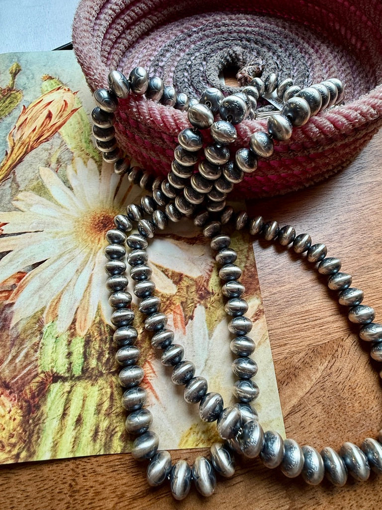 Silver beaded necklace on a textured surface with floral paper