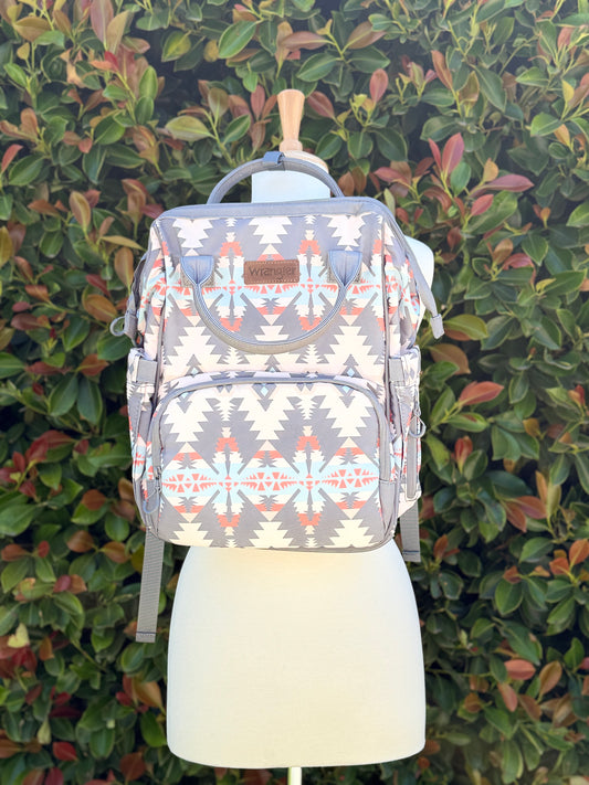 A gray backpack with Aztec geometric patterns displayed on a mannequin against a foliage background.