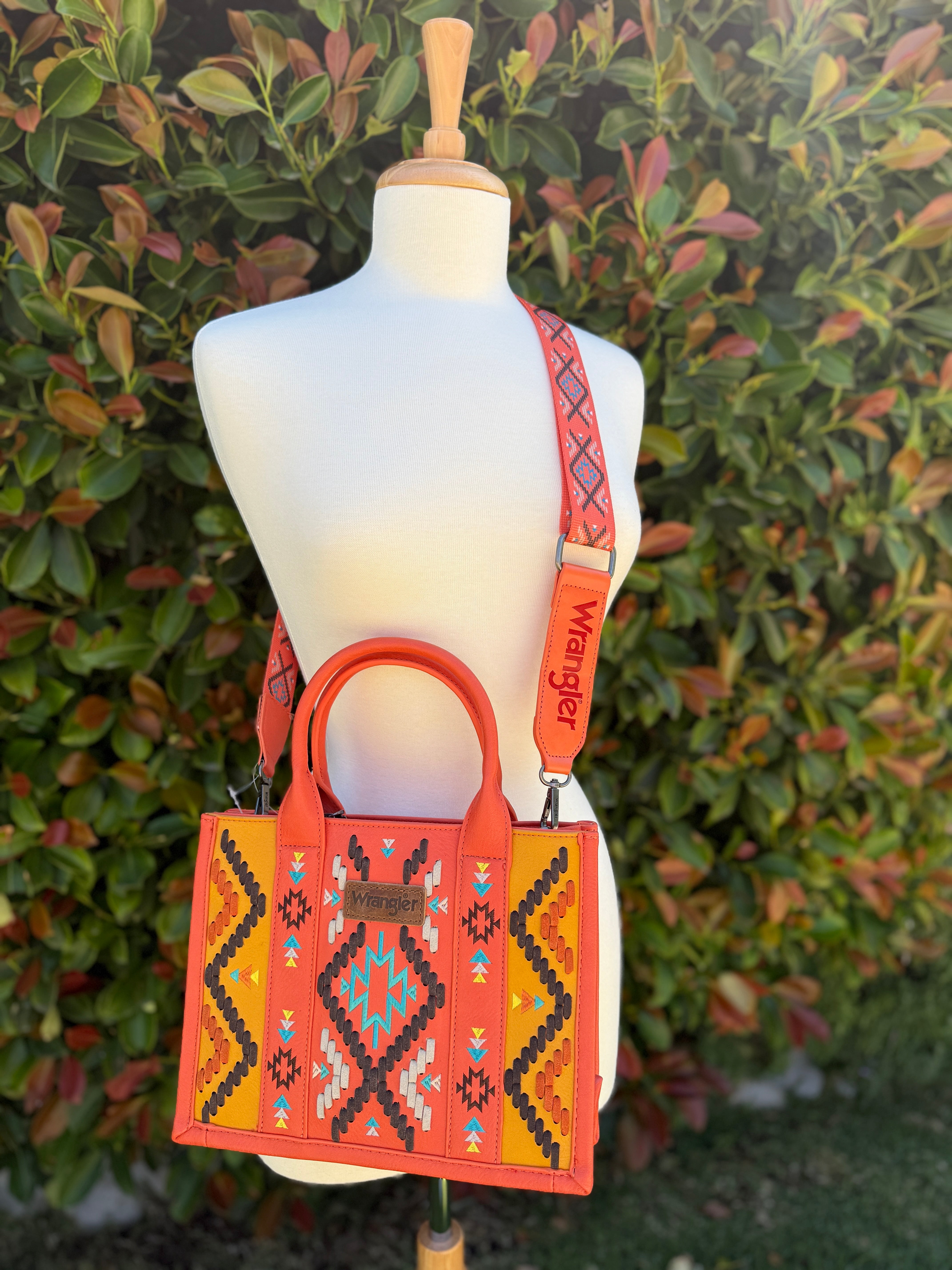 An orange Wrangler Aztec embroidered tote/crossbody bag with a geometric pattern displayed on a mannequin.