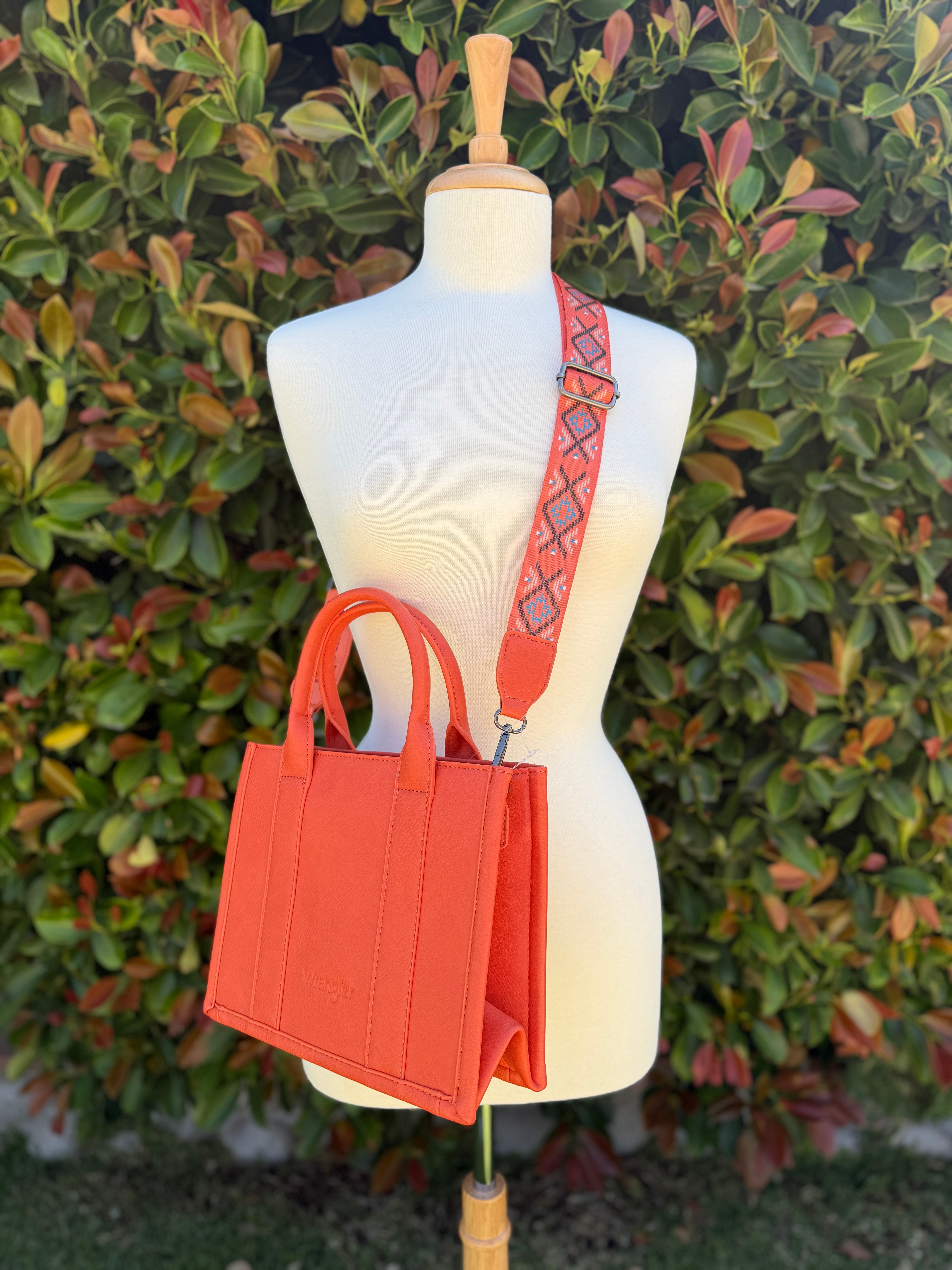An orange Wrangler Aztec embroidered tote/crossbody bag with a geometric pattern displayed on a mannequin.