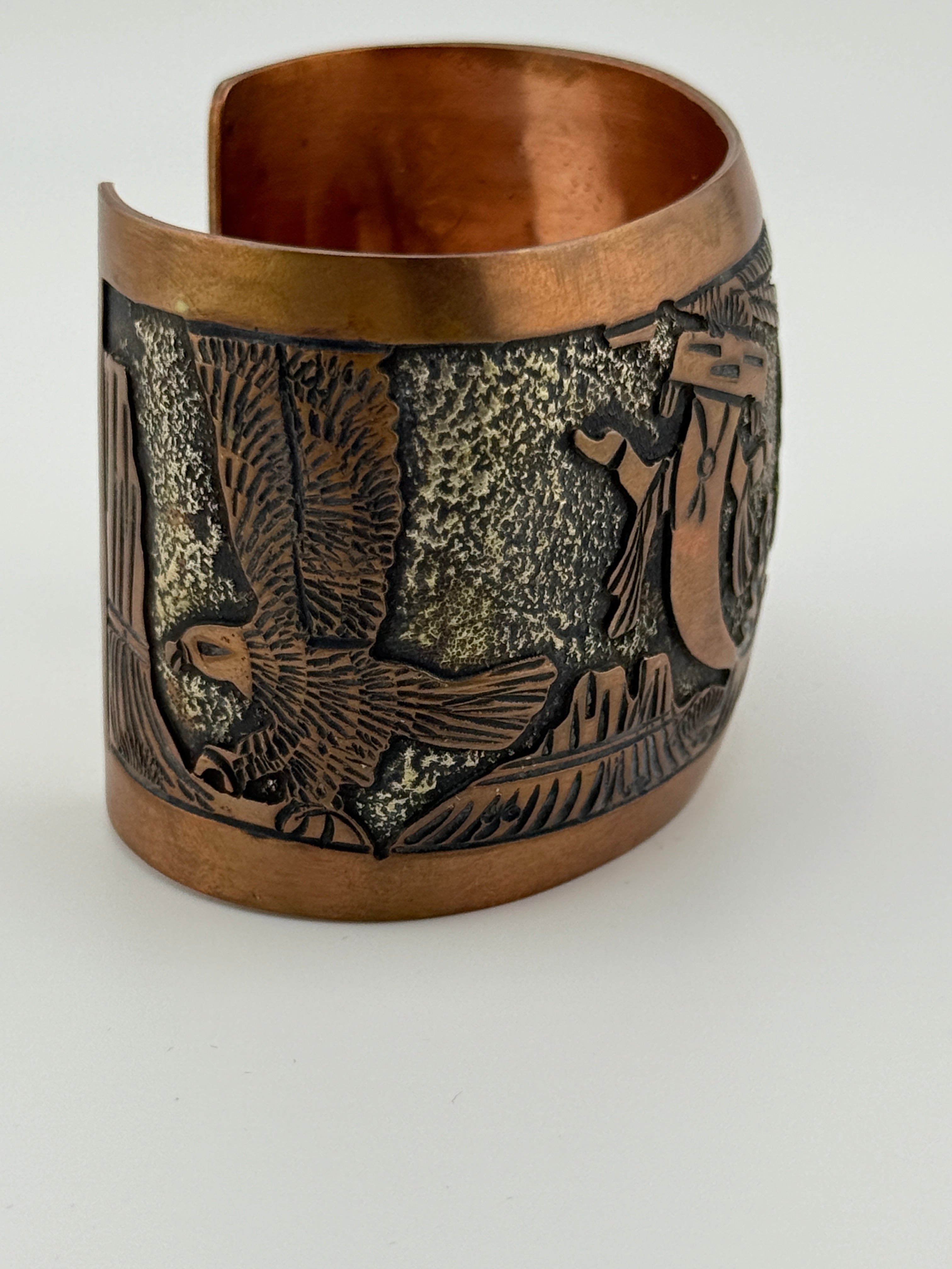 Bronze cuff bracelet with intricate designs on a white background