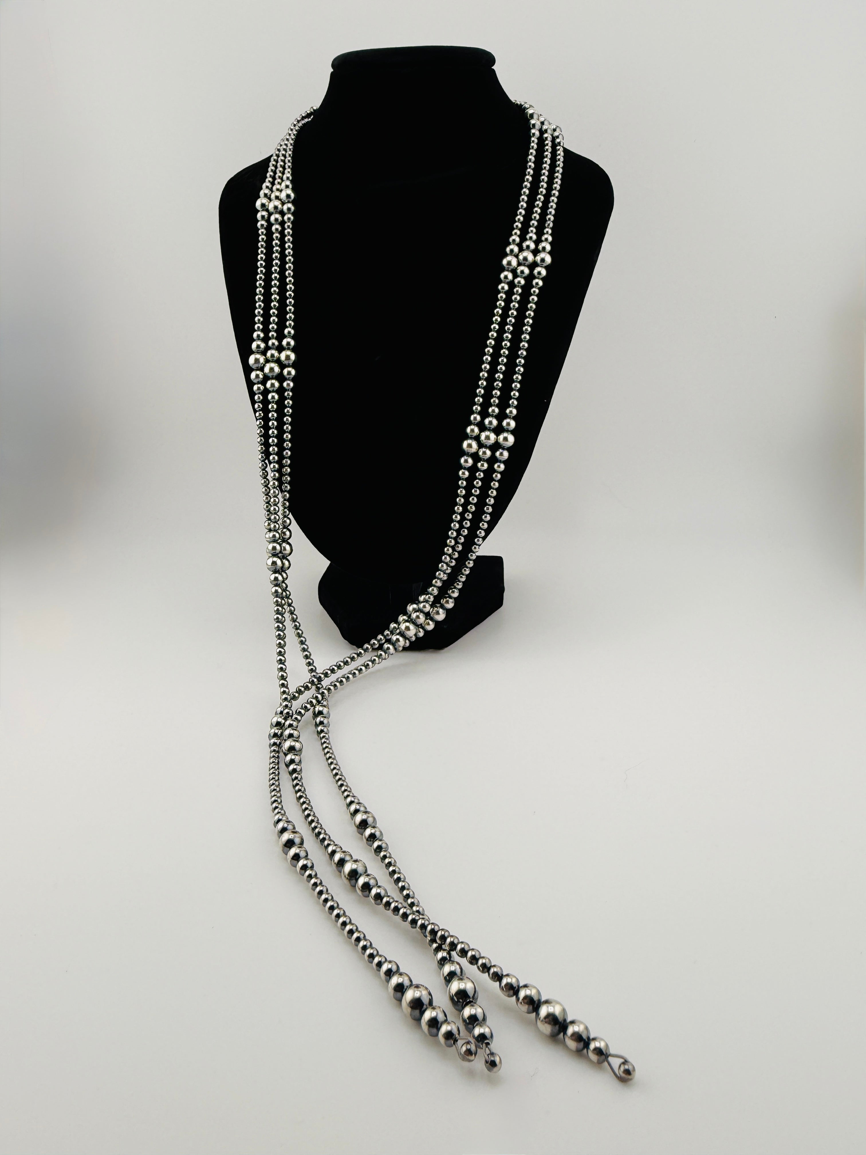 Long beaded necklace on a black mannequin bust against a white background