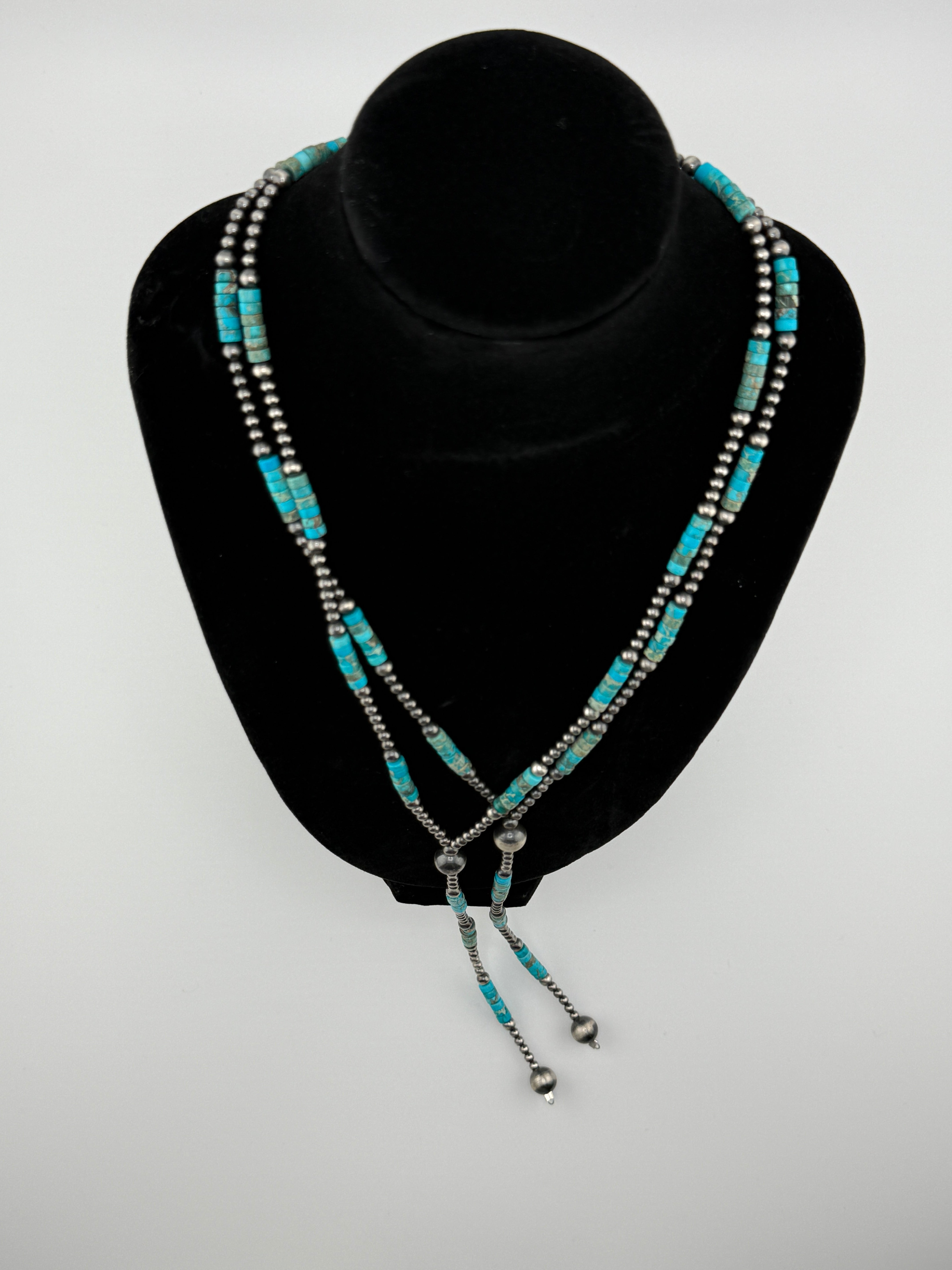 Turquoise beaded necklace on a black stand against a gray background