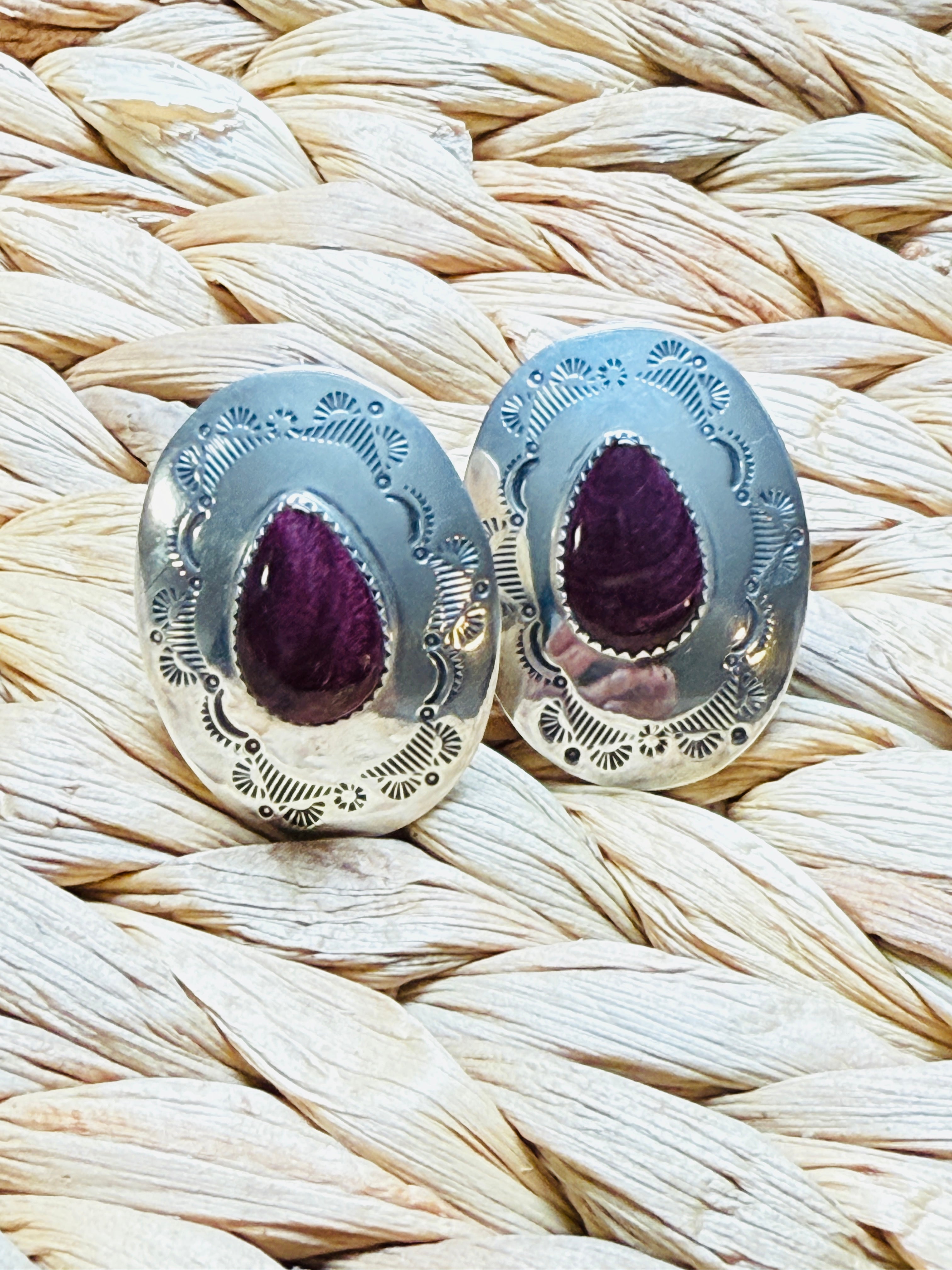 Pair of silver earrings with purple gemstones on a woven surface