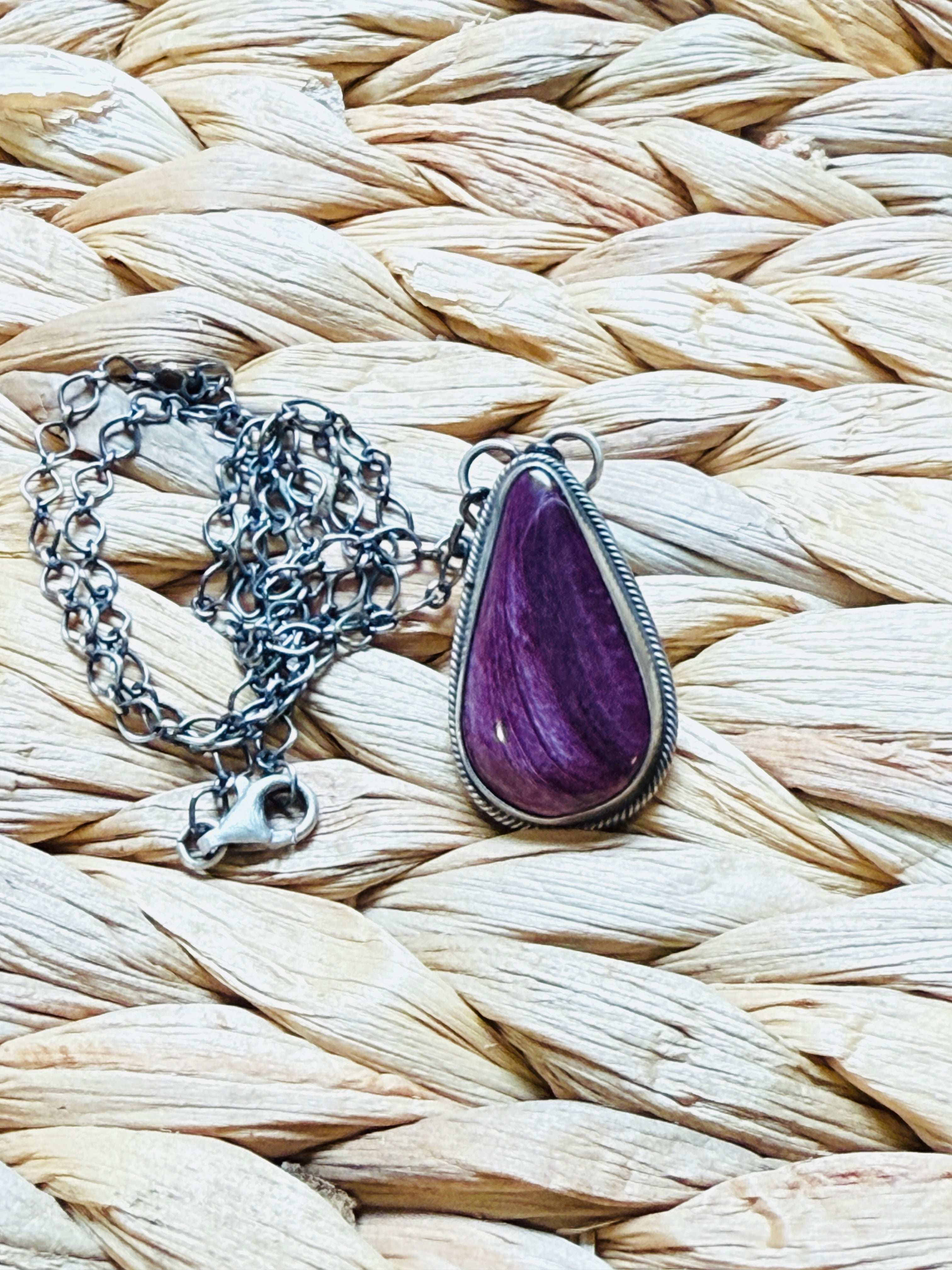 Necklace with a purple teardrop pendant on a woven surface