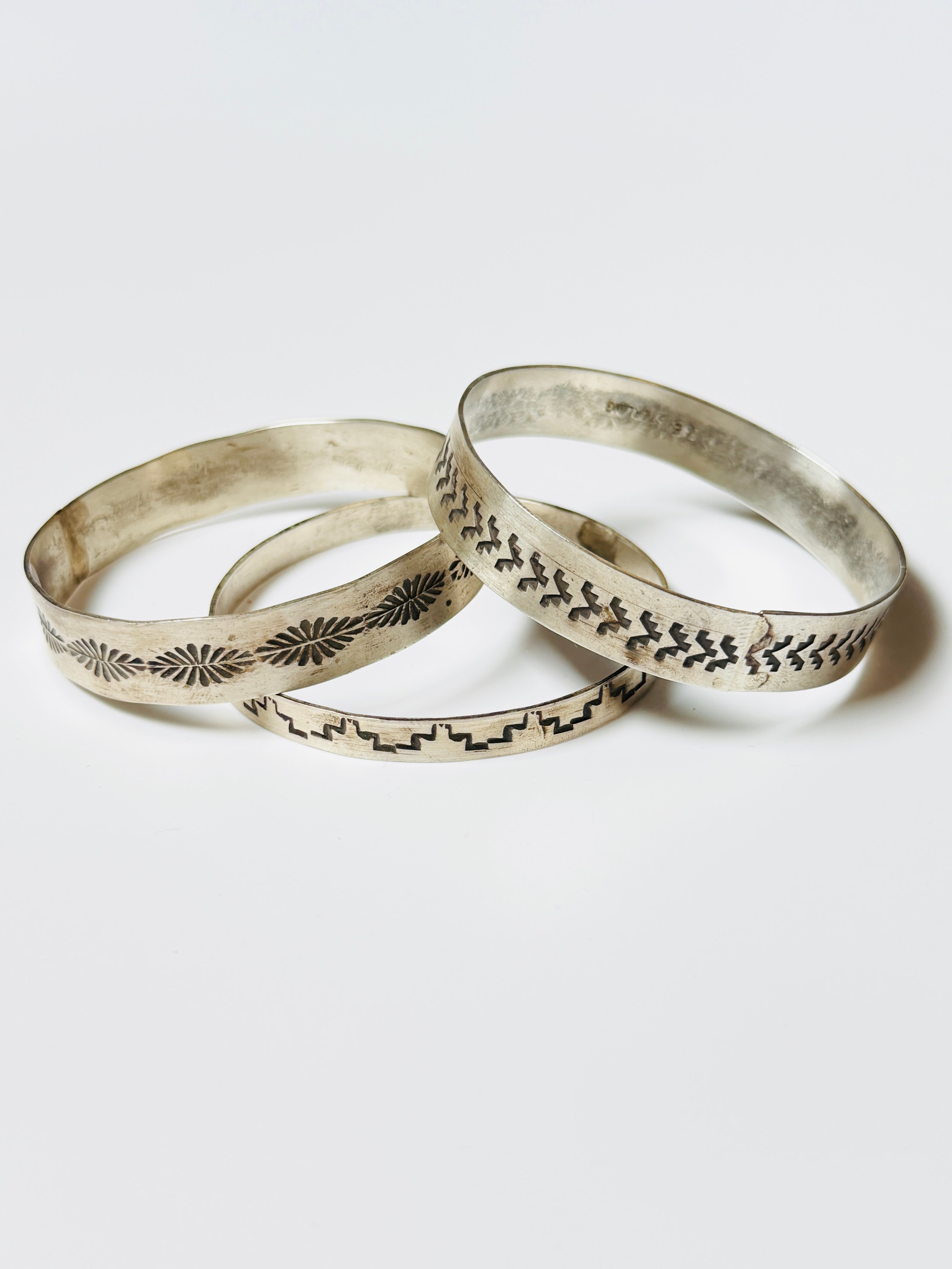Three silver bangles with engraved patterns on a white background