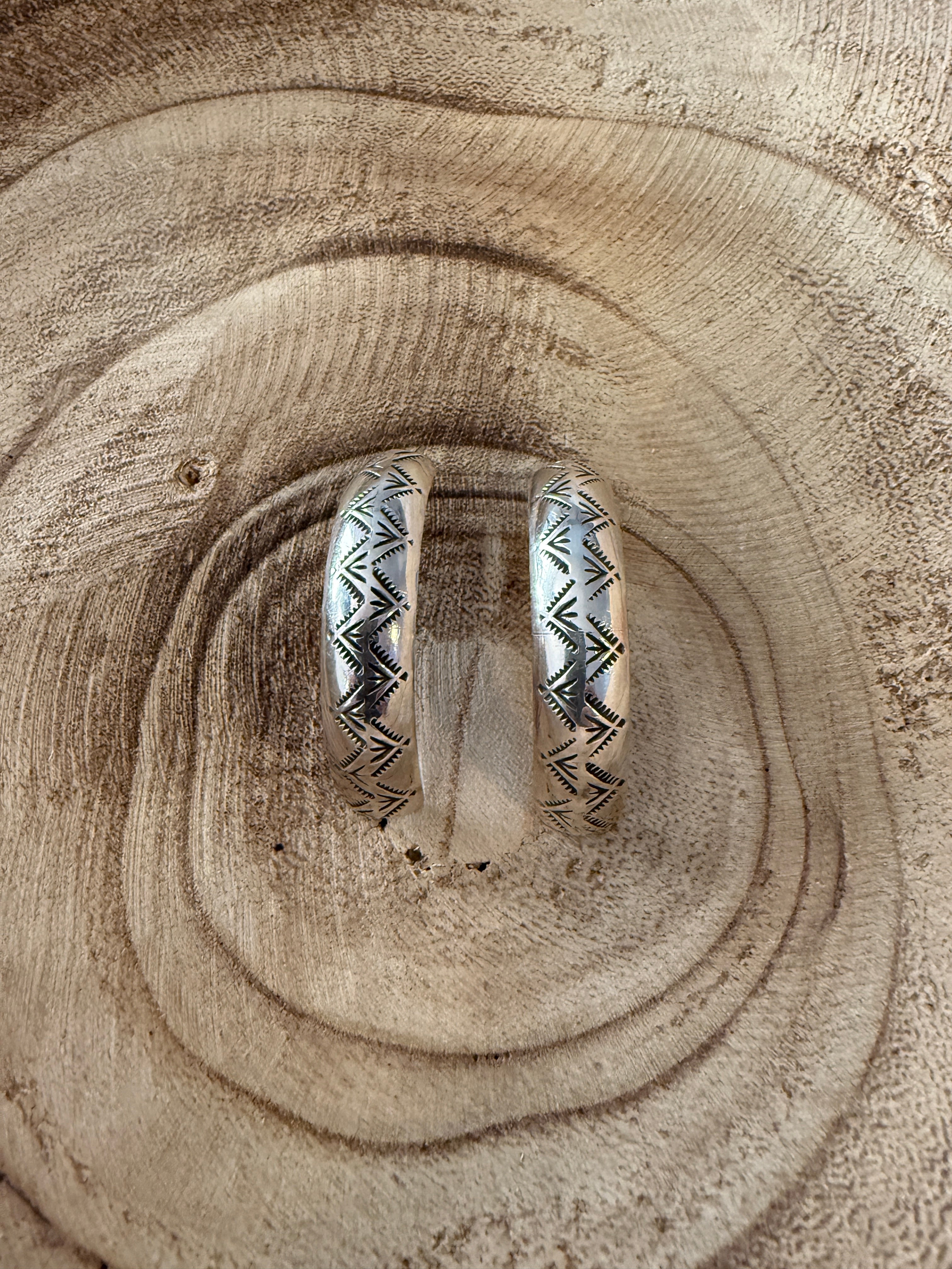Silver hoop earrings with tribal patterns on a wooden surface