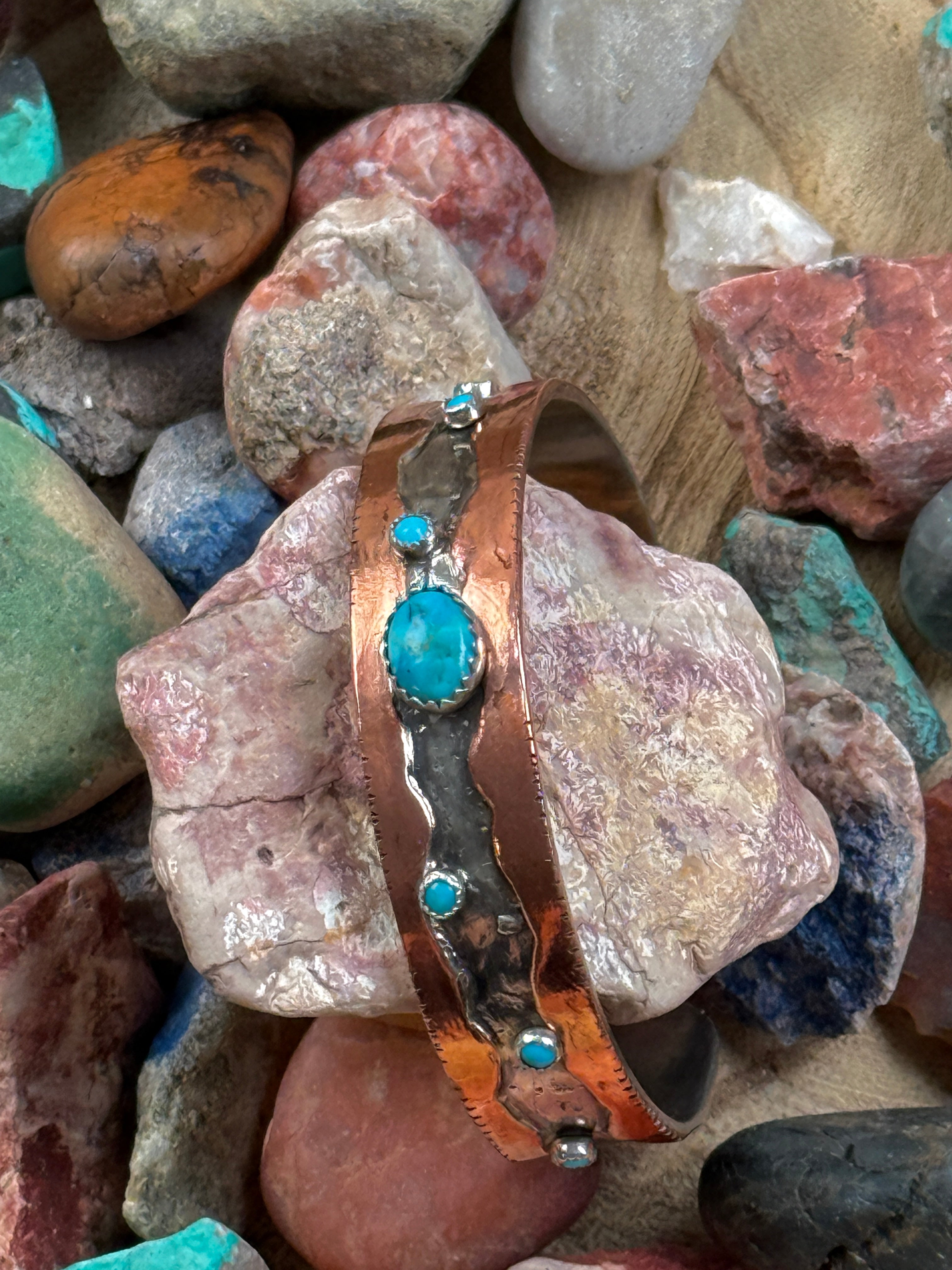 Copper bracelet with turquoise stones on a bed of multicolored stones