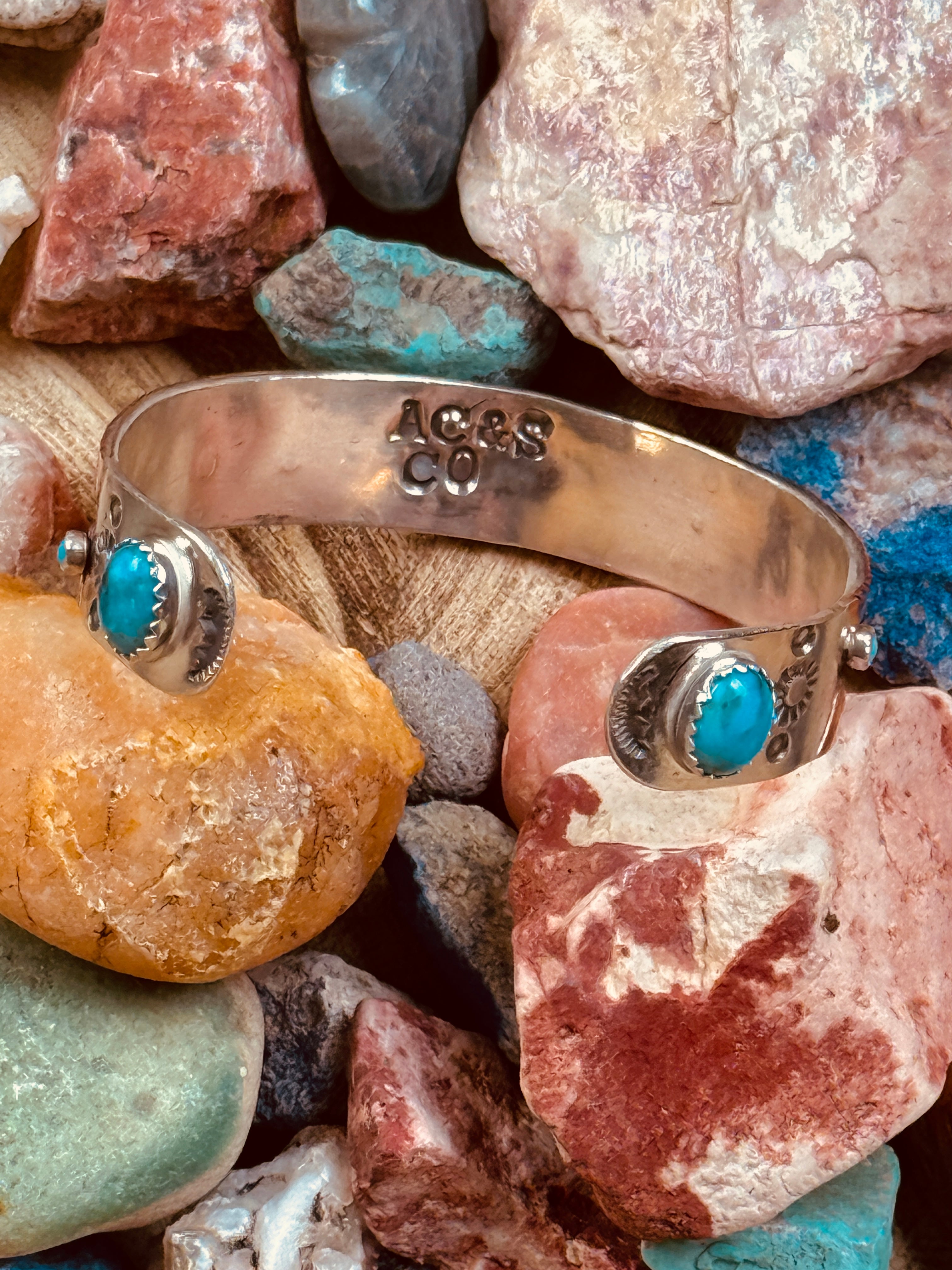 Silver bracelet with turquoise stones on a pile of multicolored stones
