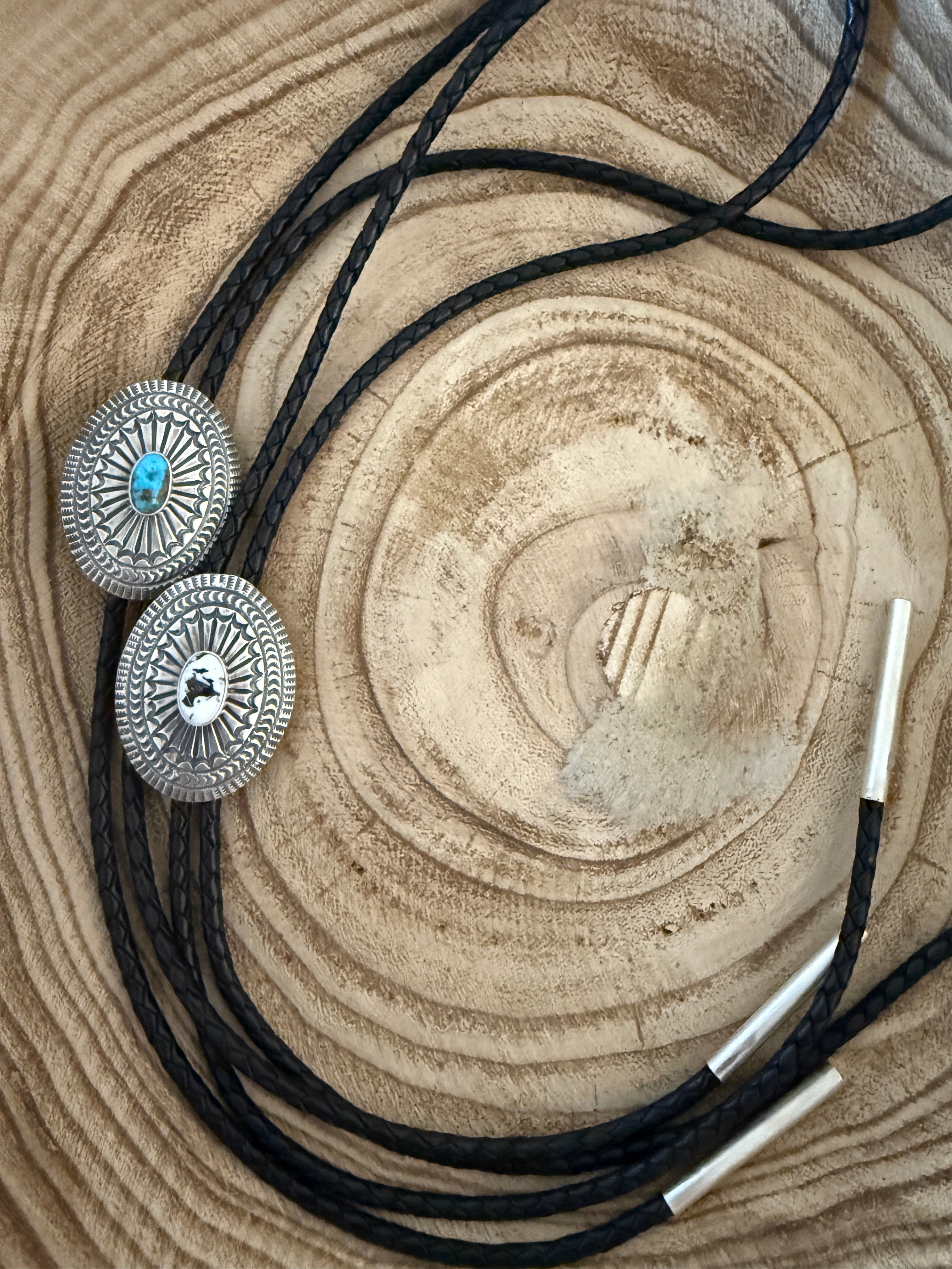 Bolo tie with silver conchos and turquoise stone on a wooden surface