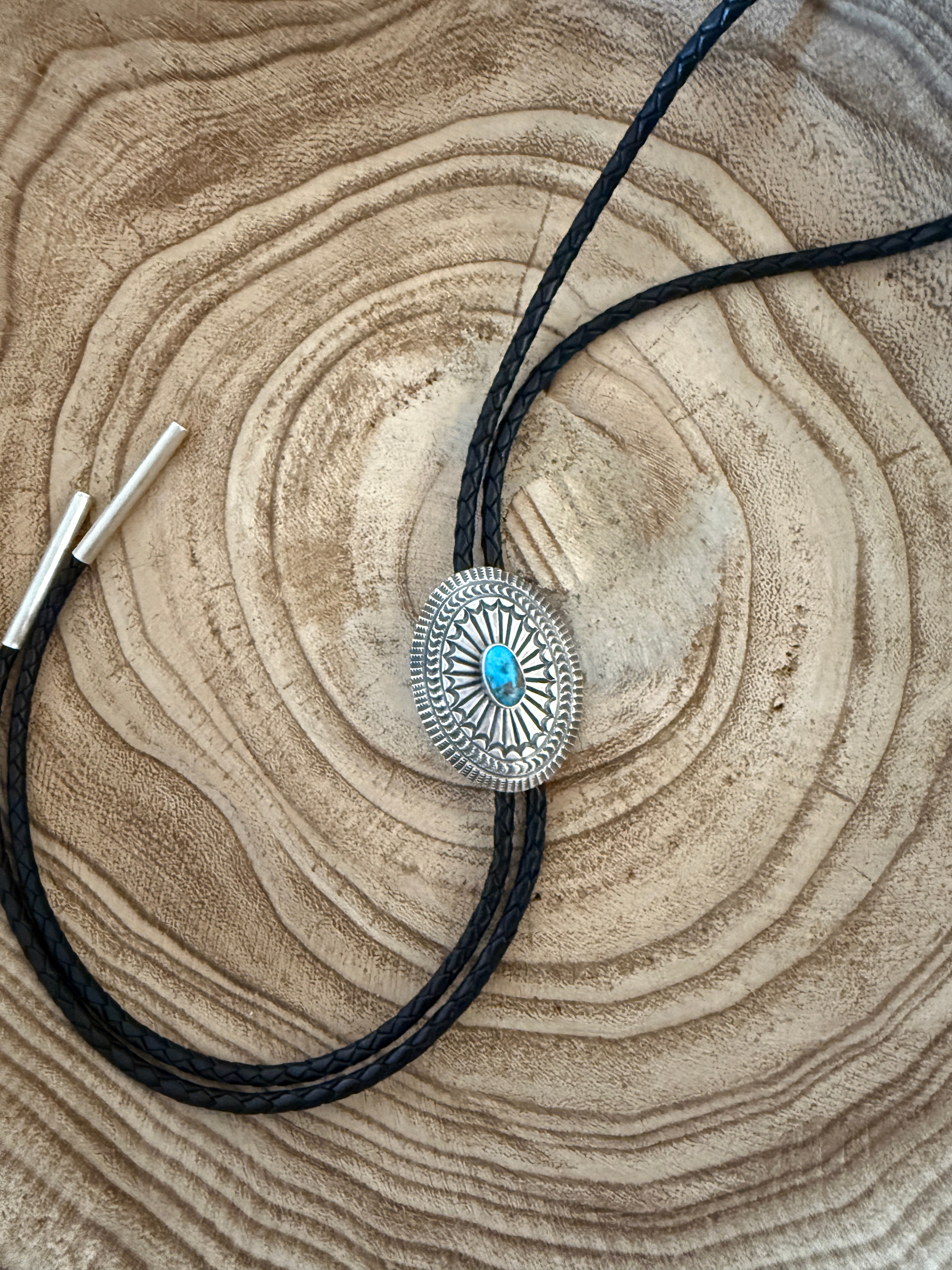 Bolo tie with a silver clasp and turquoise stone on a wooden surface