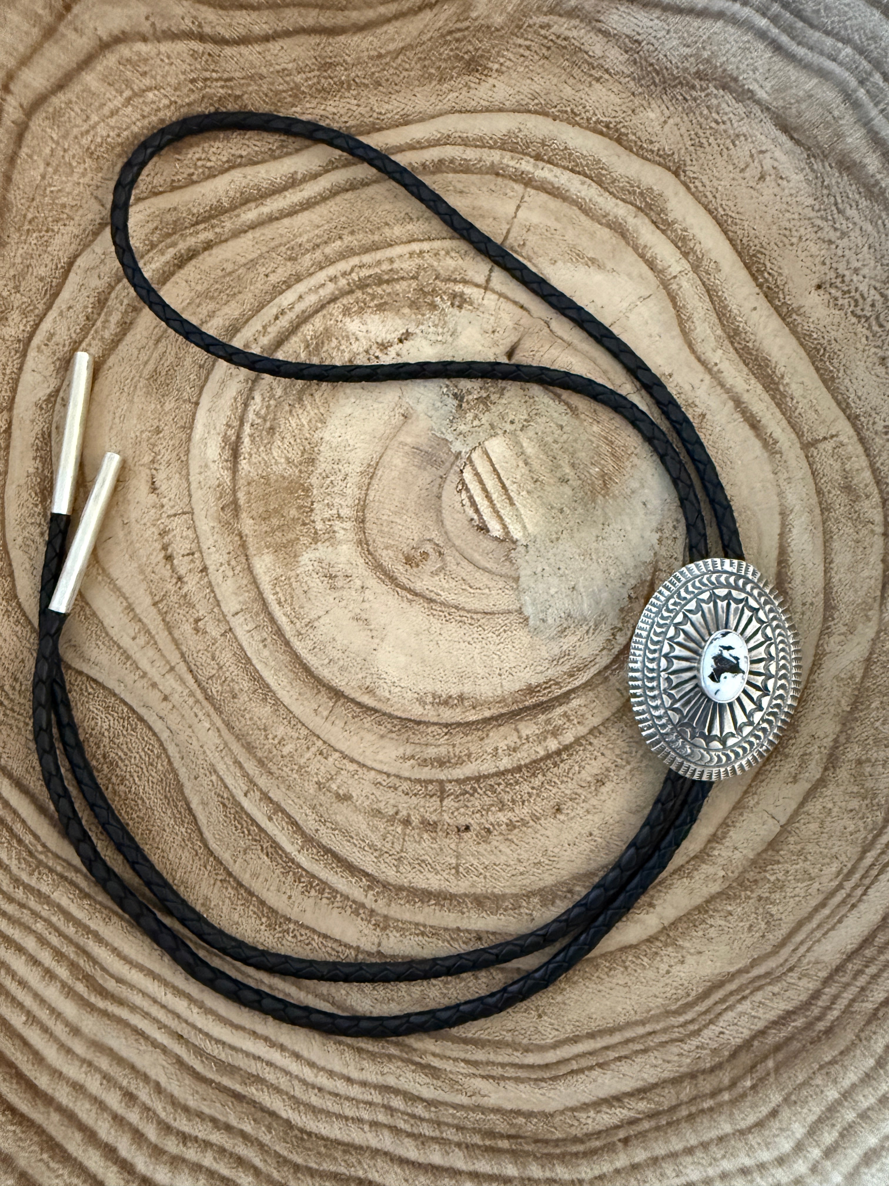 Silver bolo tie on a black cord with a textured wooden surface background