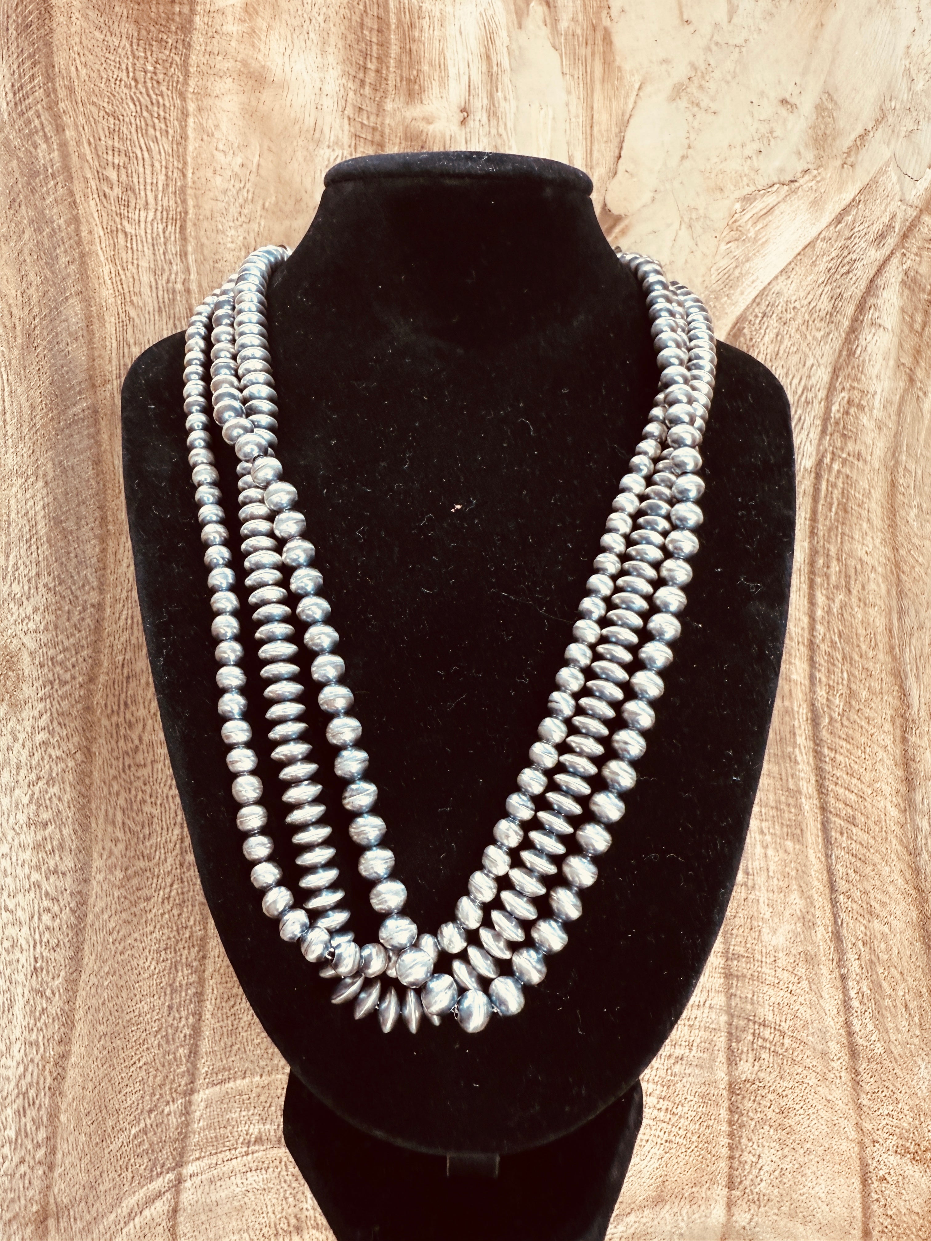 Multiple strands of pearls on a black mannequin against a wooden background