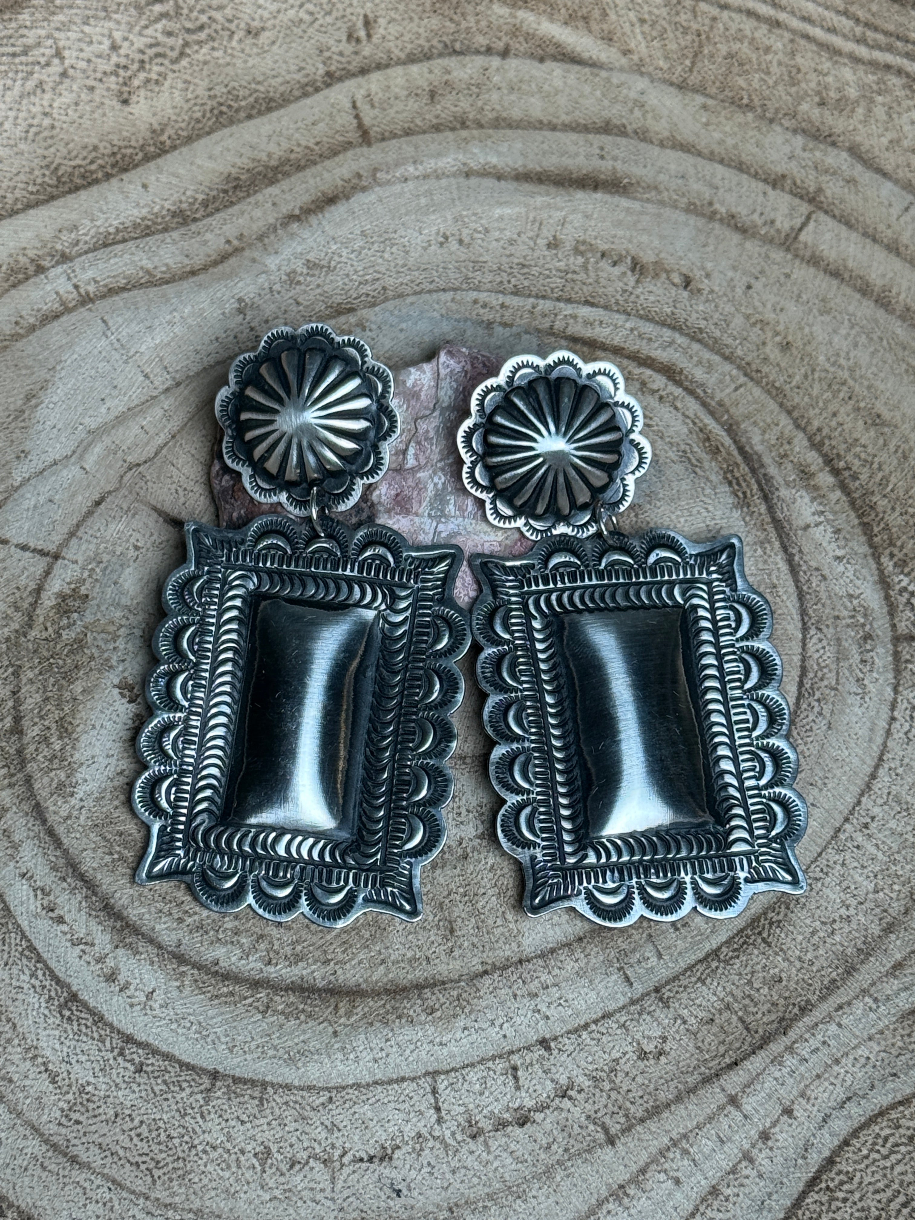 Two silver concho-style belt buckles on a textured beige surface