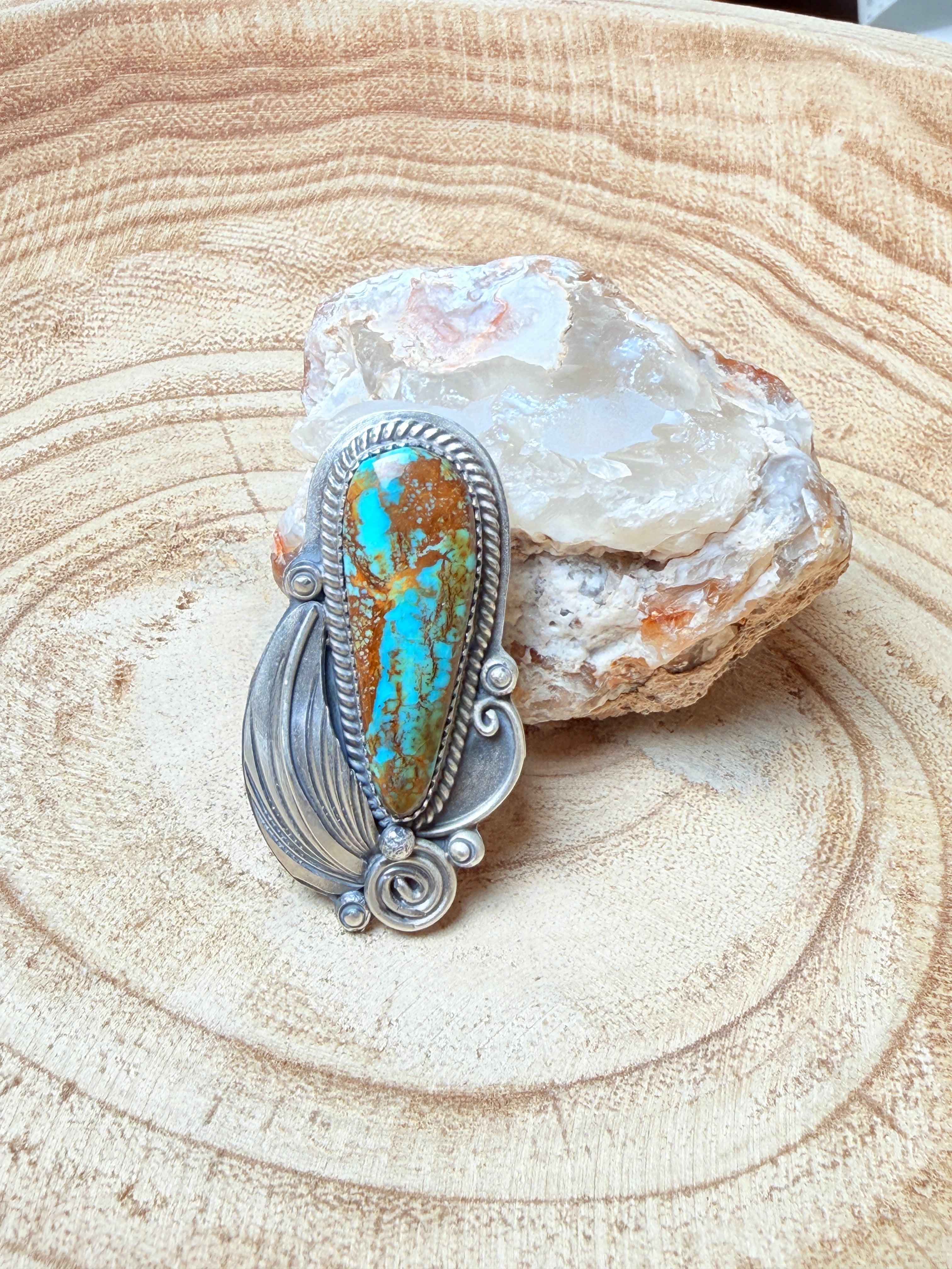 Silver ring with turquoise stone on a crystal and wooden surface