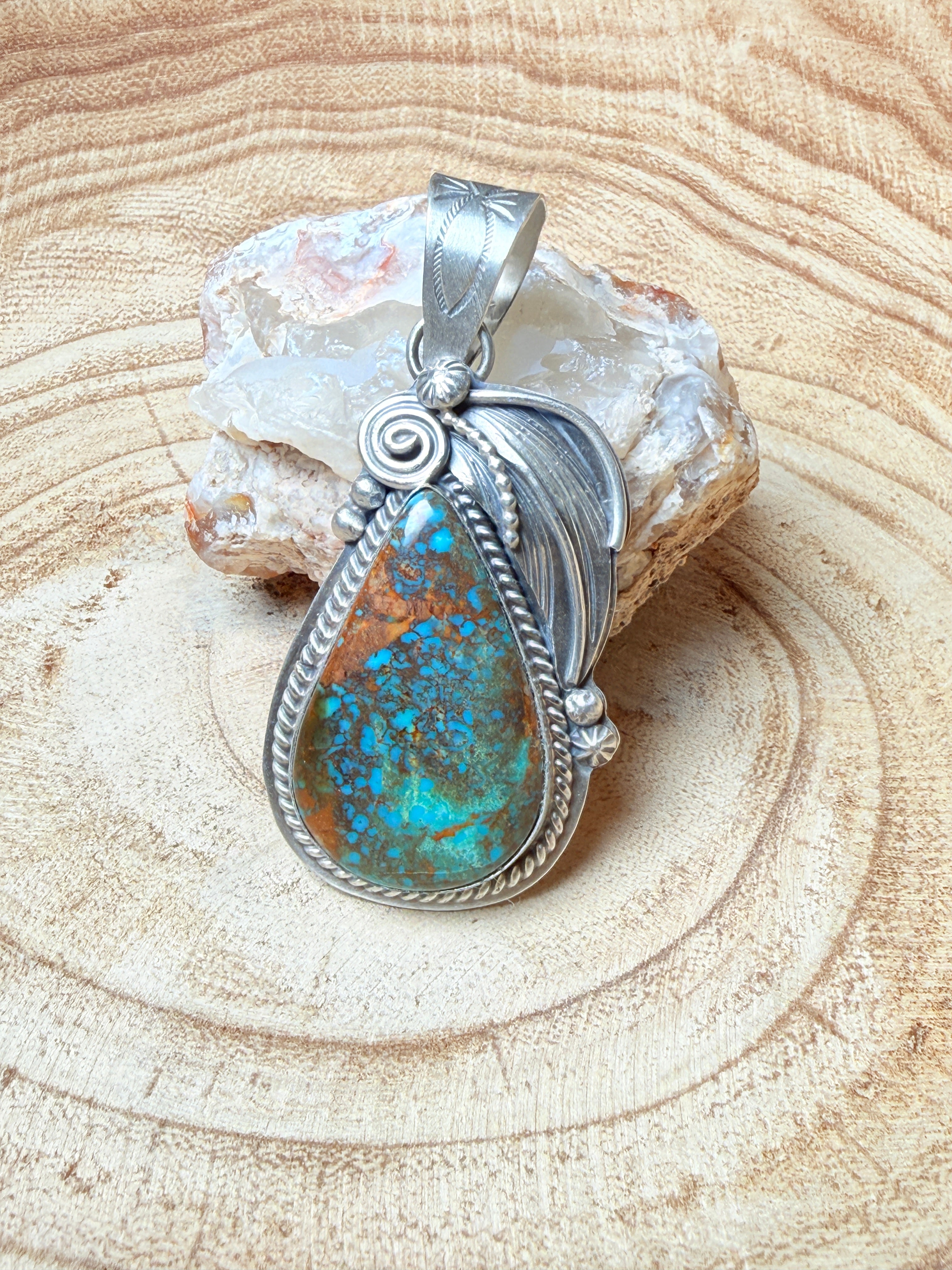 Silver pendant with a blue-green stone on a wooden surface