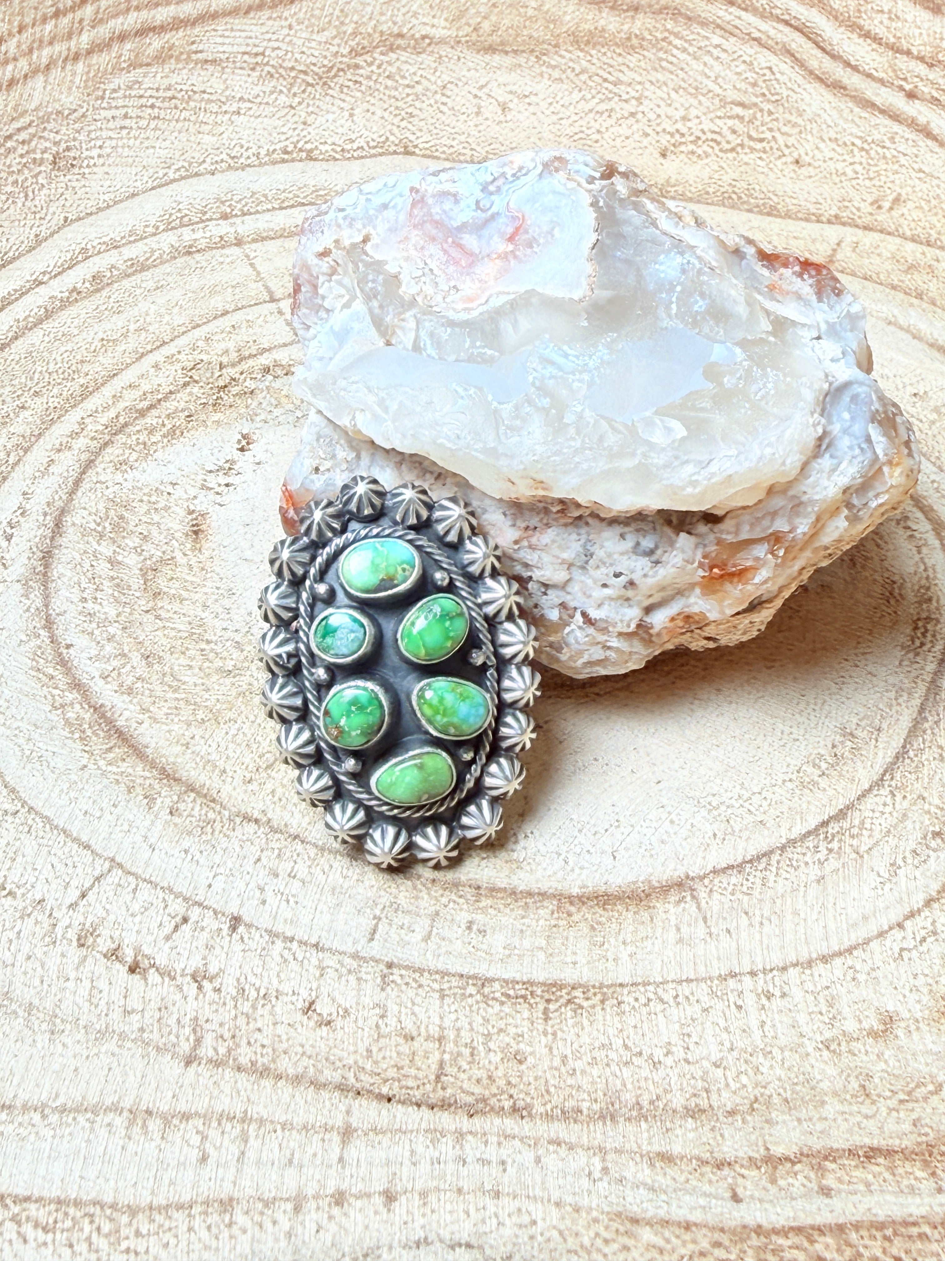 Silver ring with green gemstones on a wooden surface with a crystal