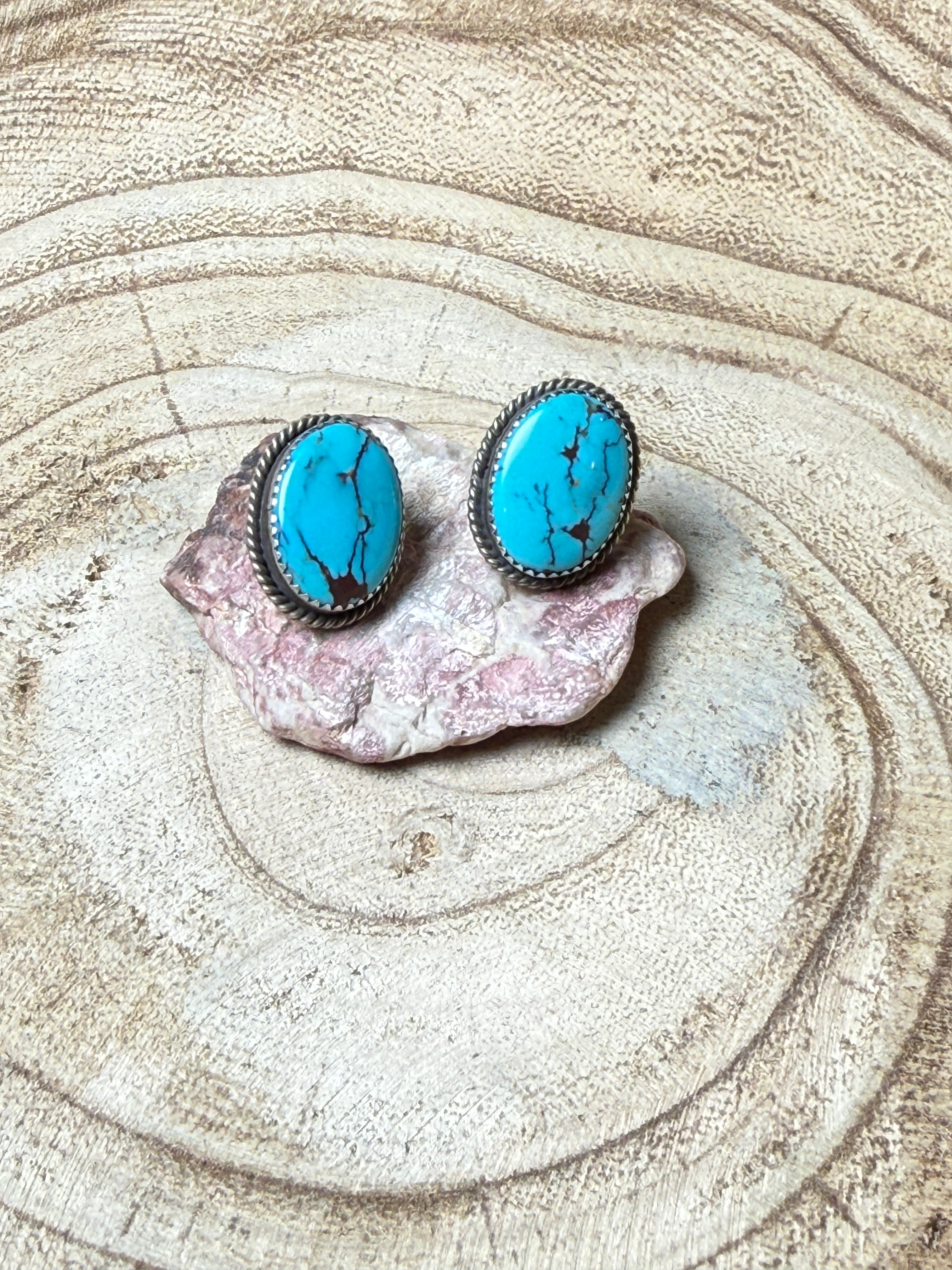 Turquoise stone earrings on a pink shell with sand background