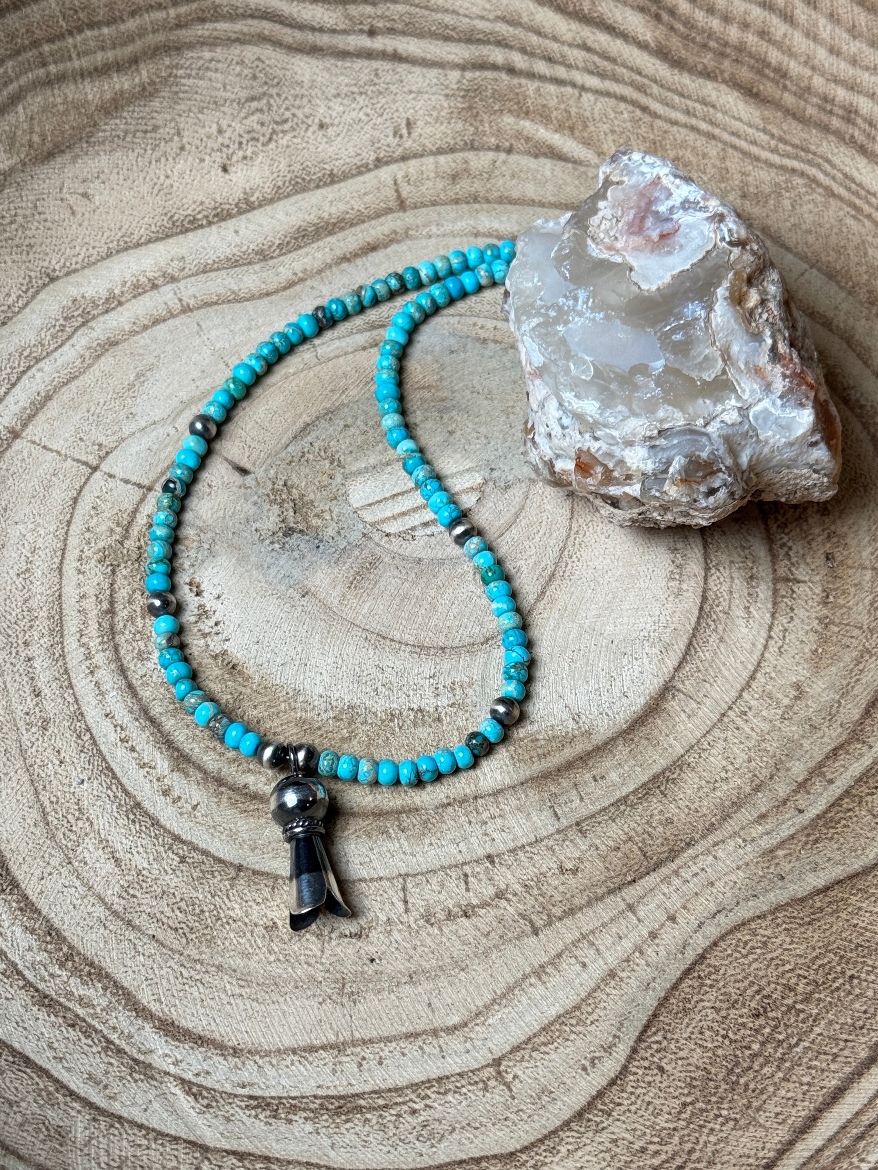Turquoise beaded necklace on a wooden surface with a crystal rock.