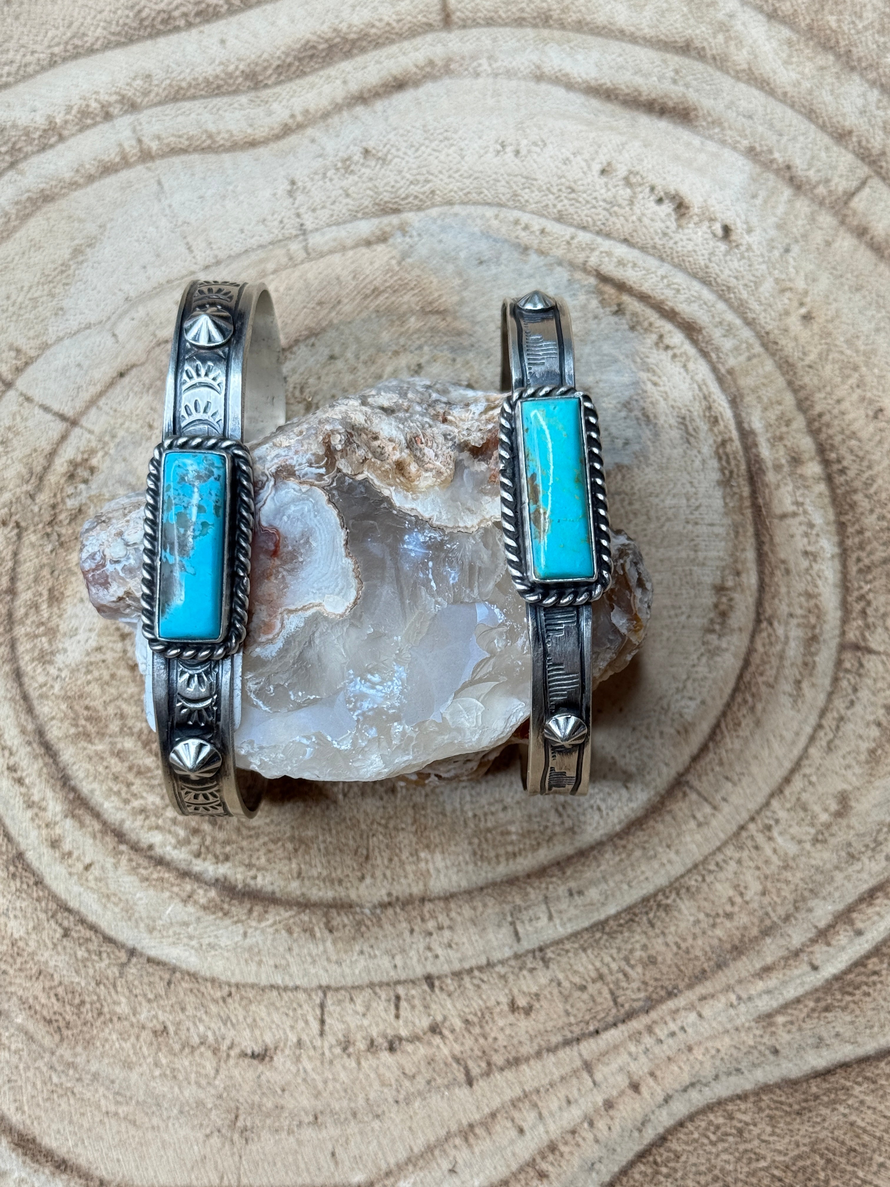 Two silver bracelets with turquoise stones on a stone surface