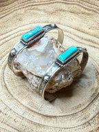 Silver cuff bracelet with turquoise accents on a crystal rock