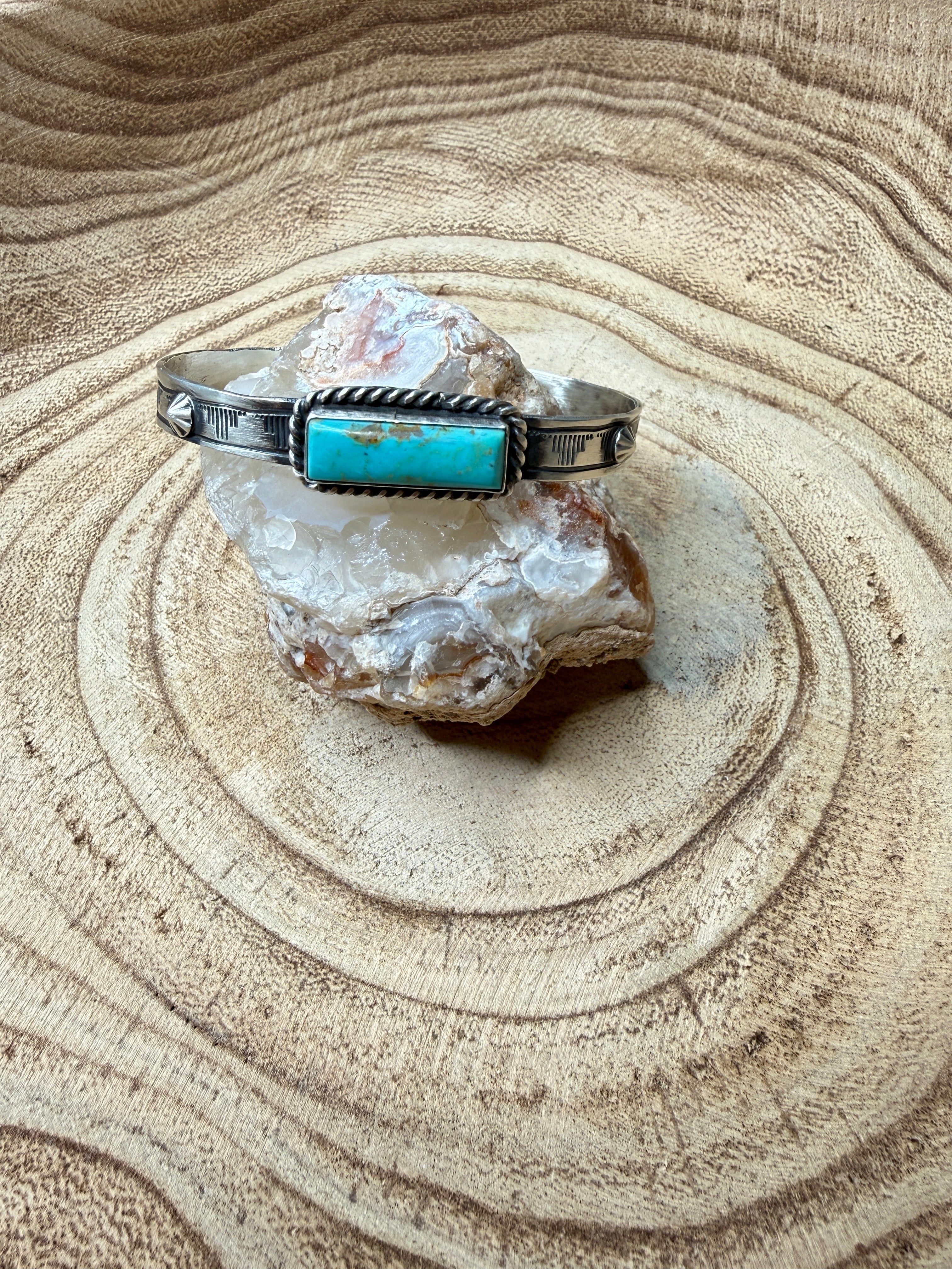 Turquoise stone with a silver bracelet on a textured surface