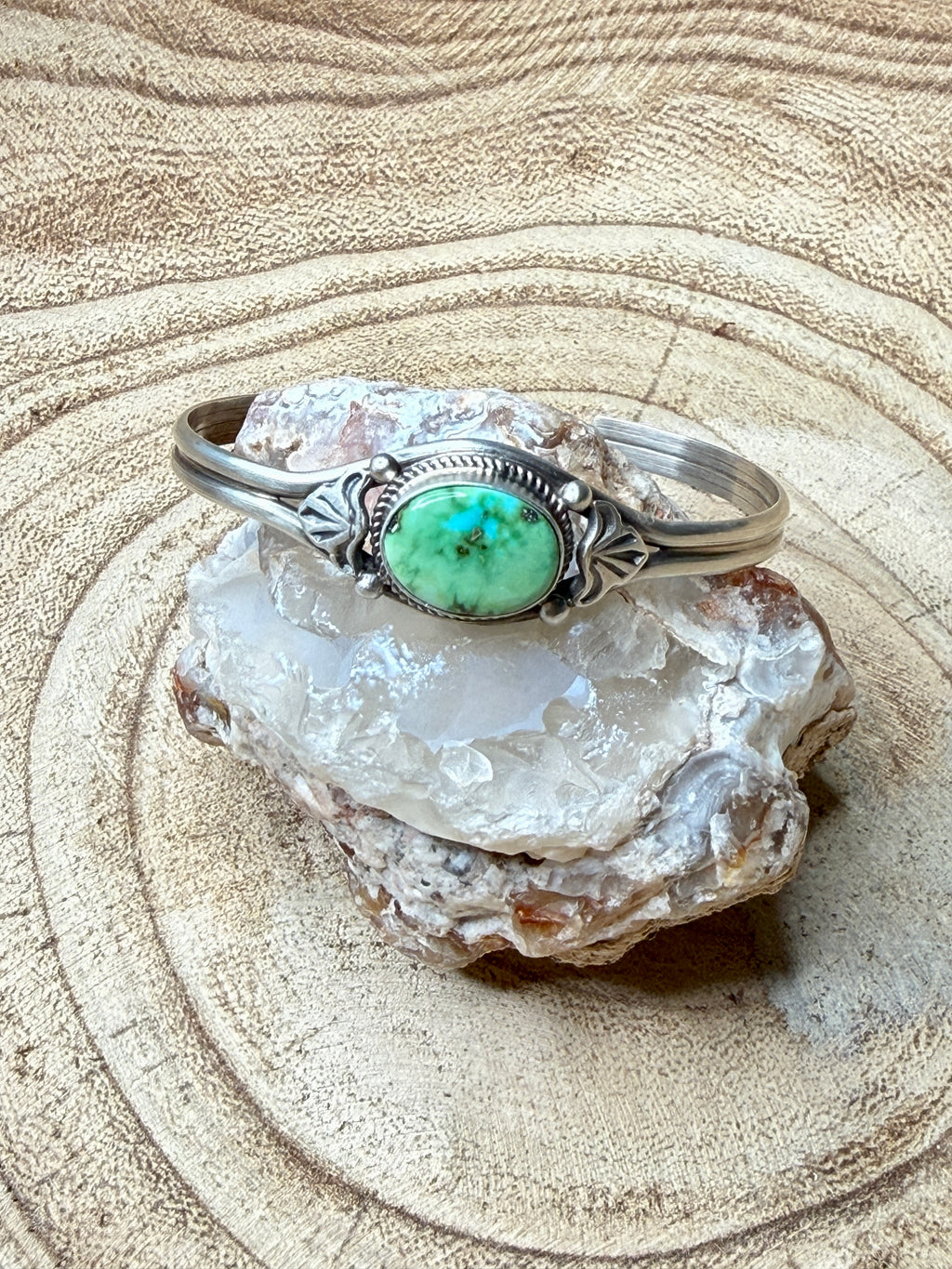 Silver bracelet with a green stone on a crystal rock against a sandy background